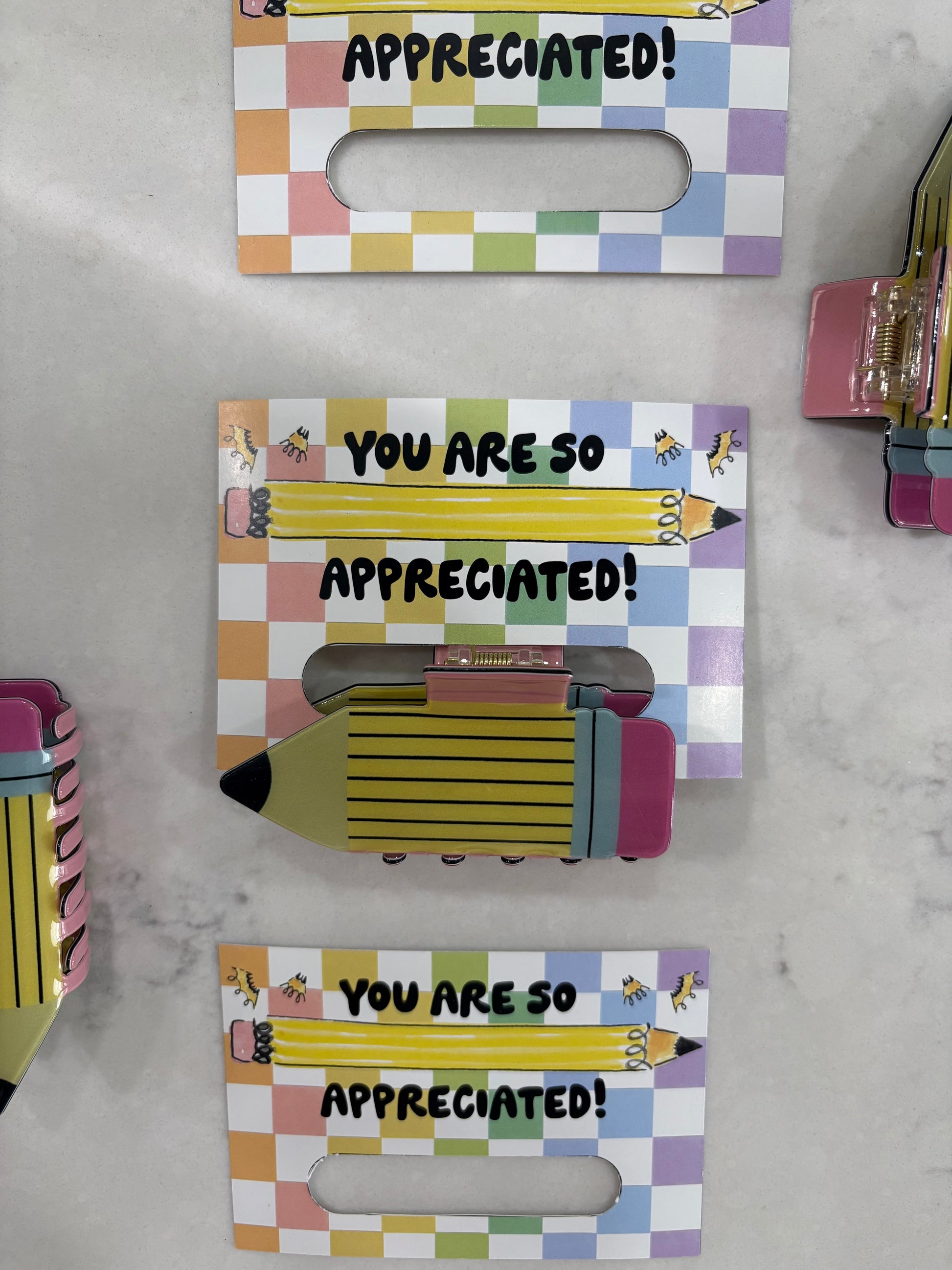 Pencil hair clips held by a colorful holder with 'You are so appreciated!' text on a marble surface