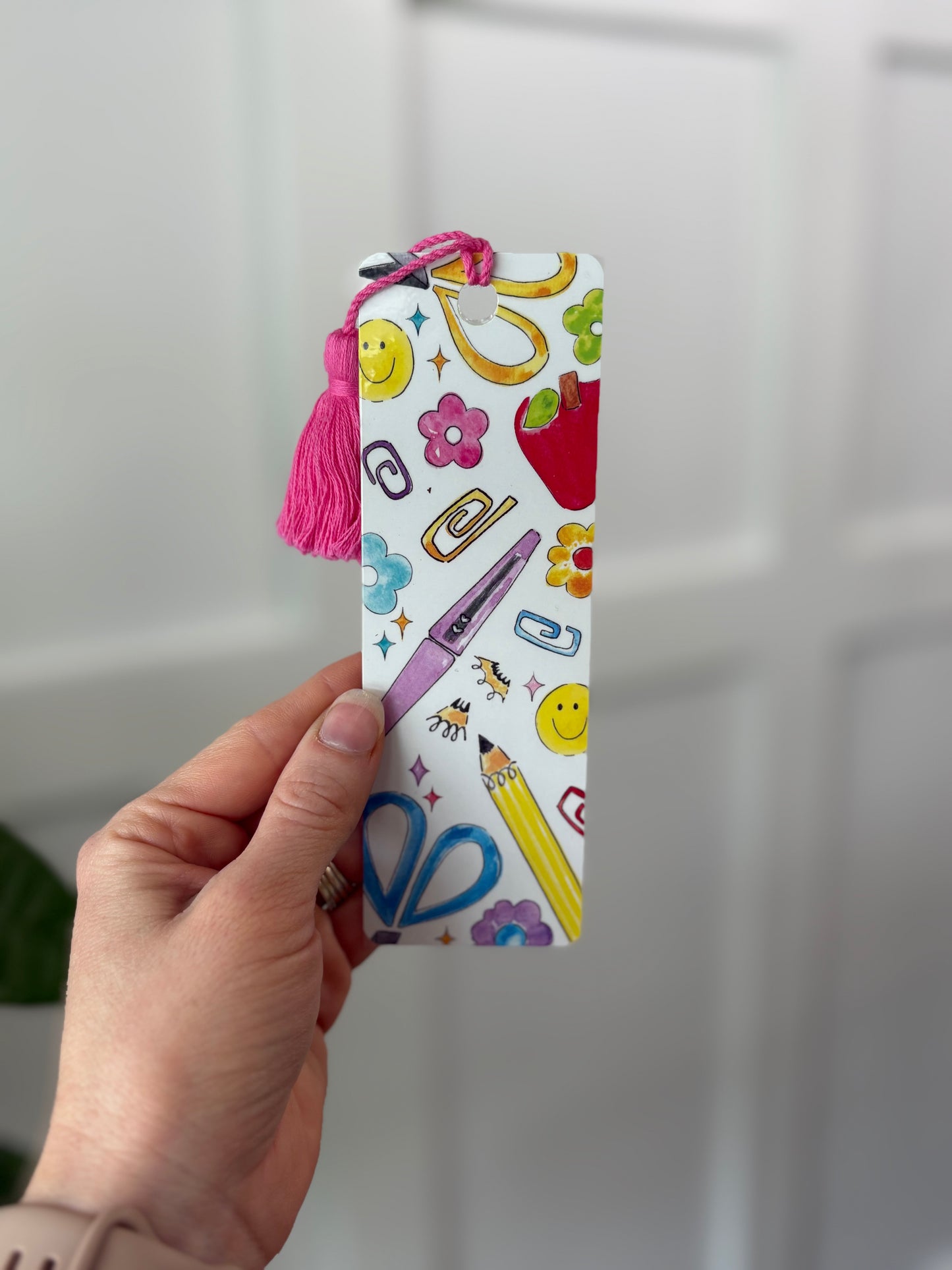 Hand holding a colorful bookmark with stationery-themed design against a white background