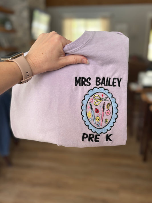 purple tshirt with 'Mrs. Bailey Pre K' text held by a person indoors.