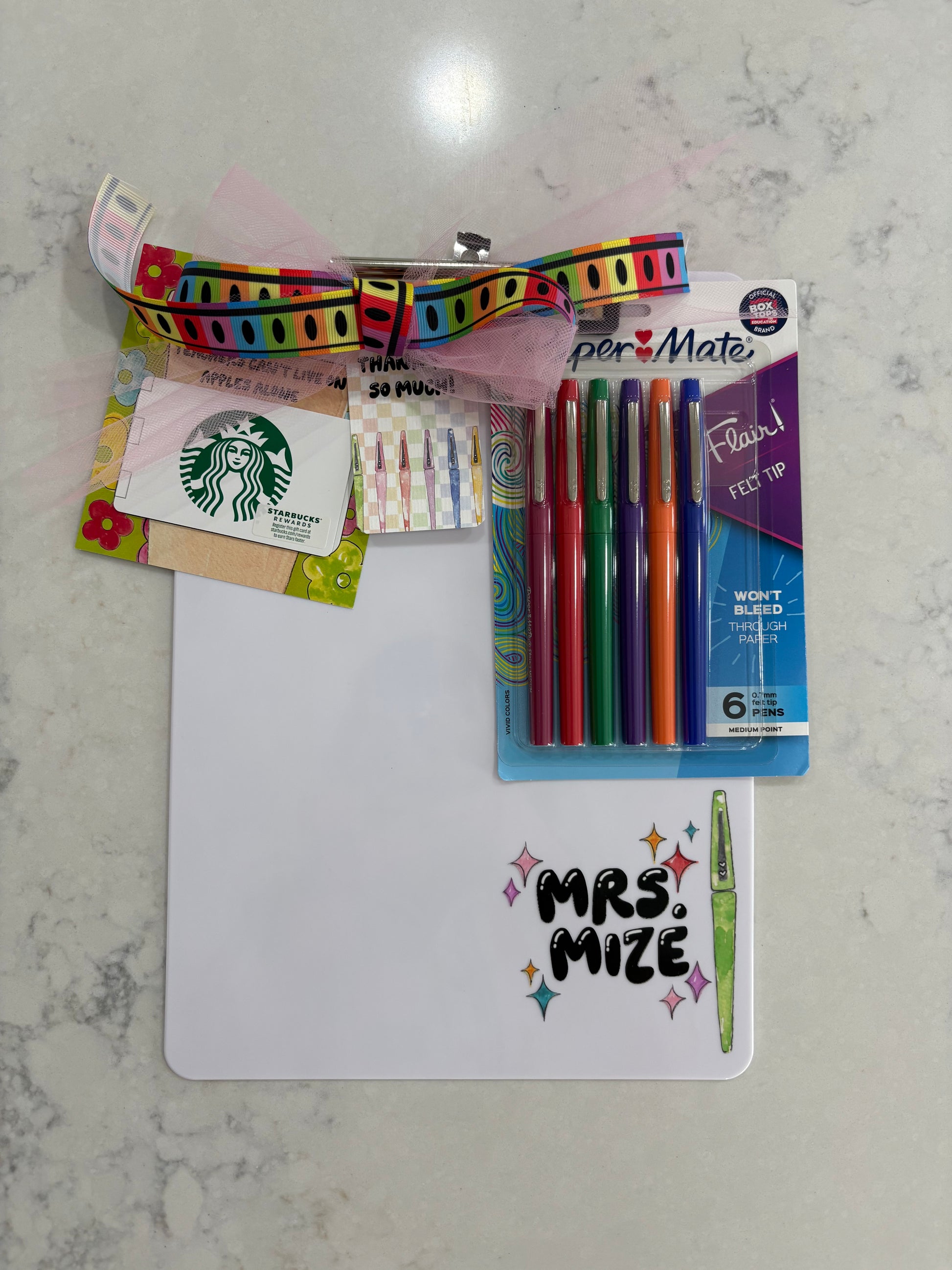Assorted stationery items including pens, a Starbucks card, and a clipboard on a marble surface.
