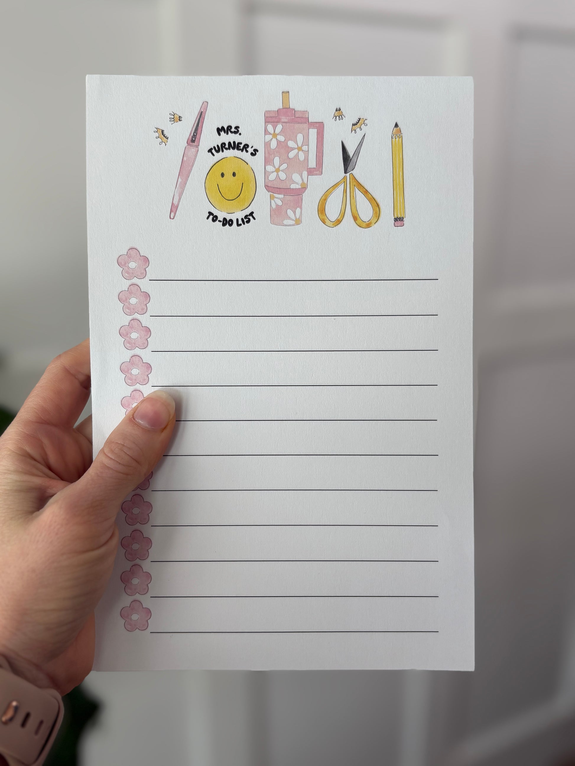 Hand holding a lined notepad with illustrations and text on a neutral background