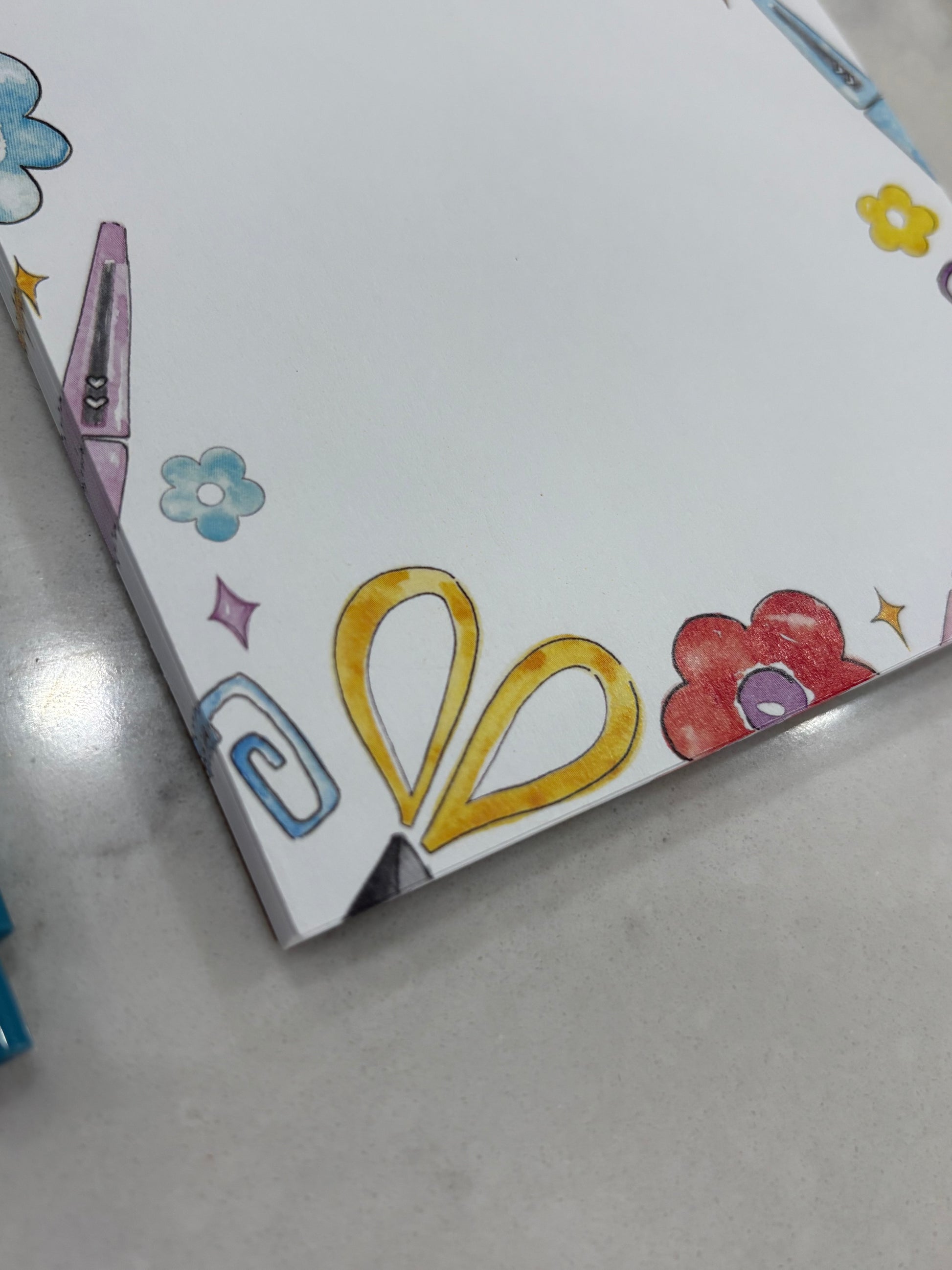 Colorful notepad with scissors and flowers on a gray surface