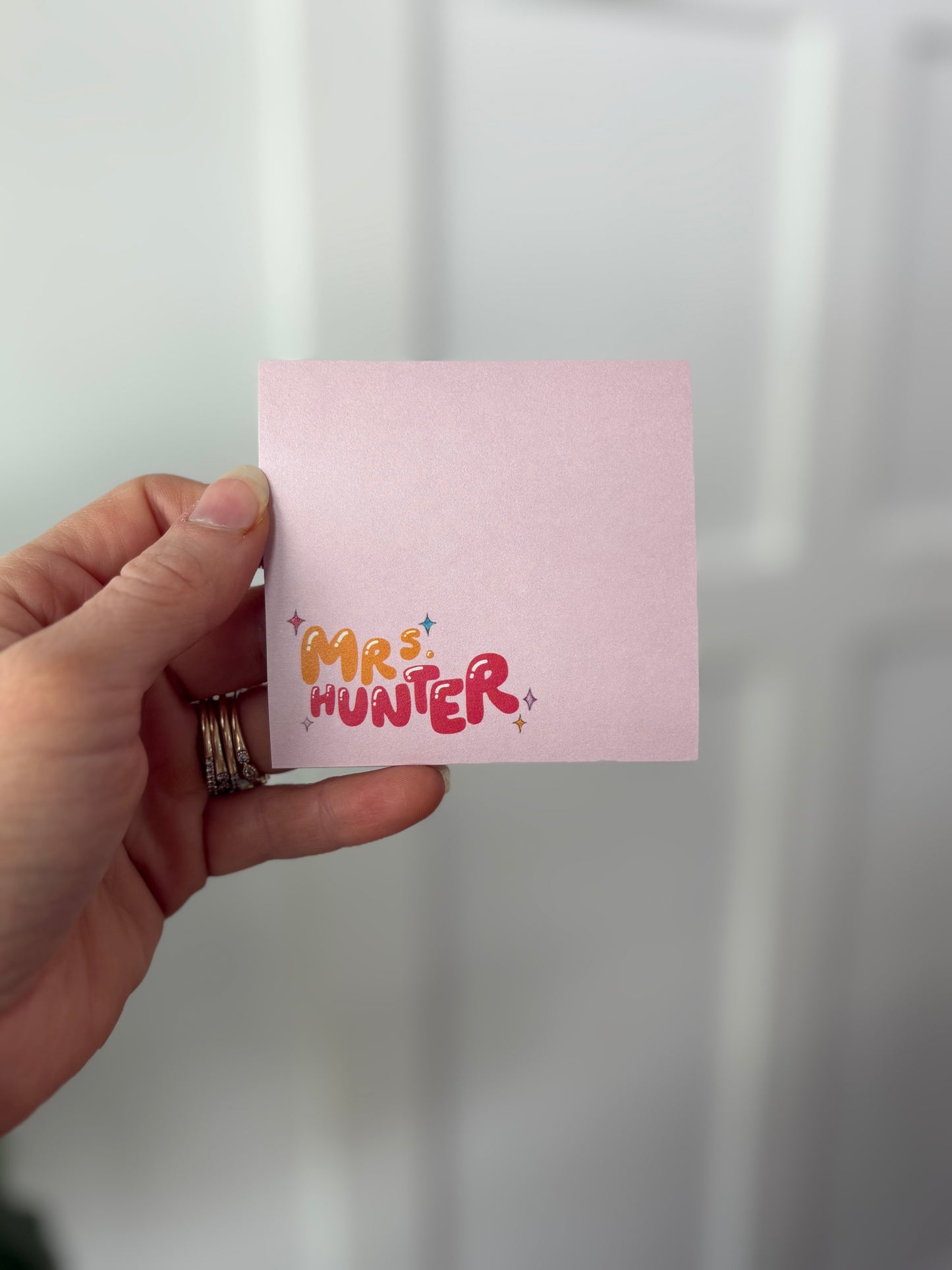 Hand holding a pink sticky notepad with 'MR. HUNTER' printed on it against a white background