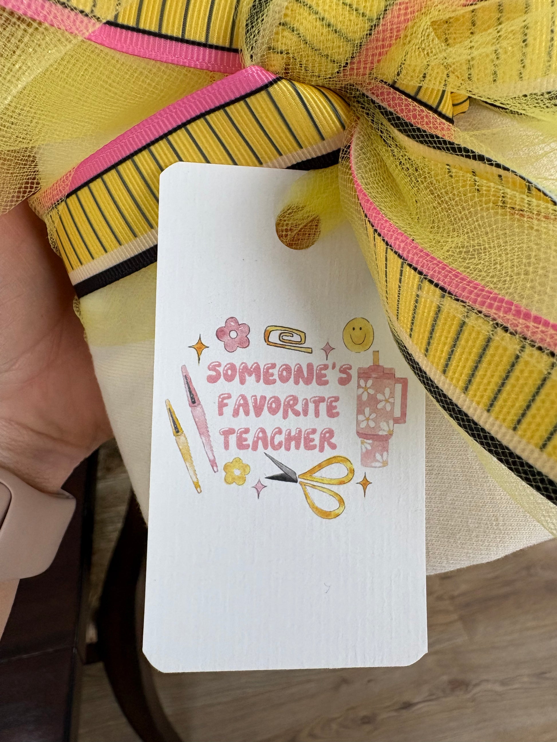 Gift tag with 'Someone's Favorite Teacher' text and illustrations, held by a yellow and pink striped bow