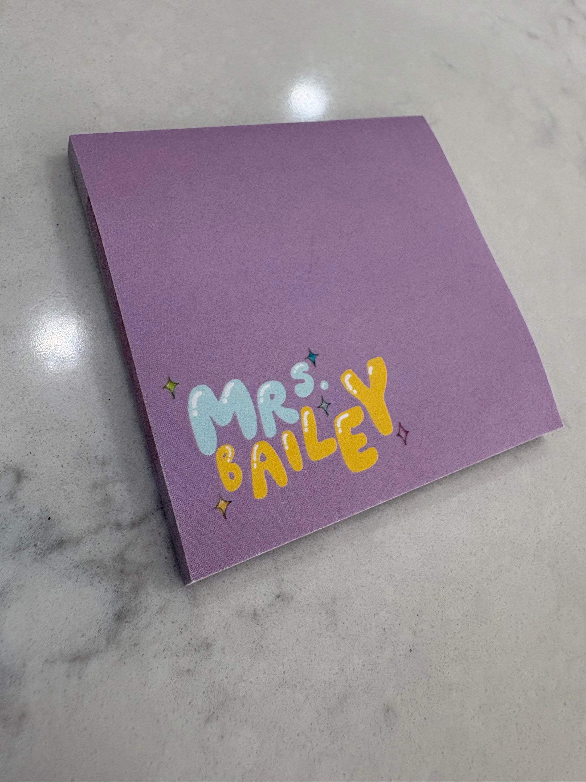 Purple sticky notebook with colorful text on a marble surface