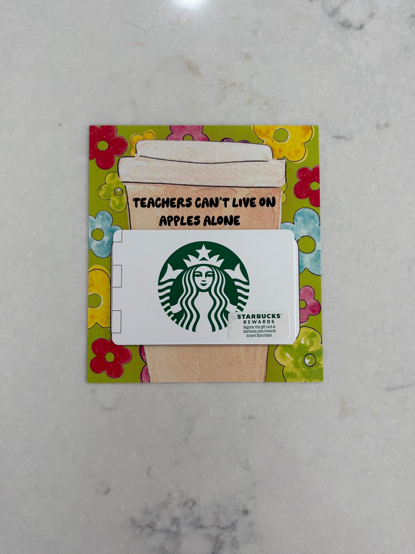 Starbucks gift card with a coffee cup design and text on a floral border, placed on a marble surface.