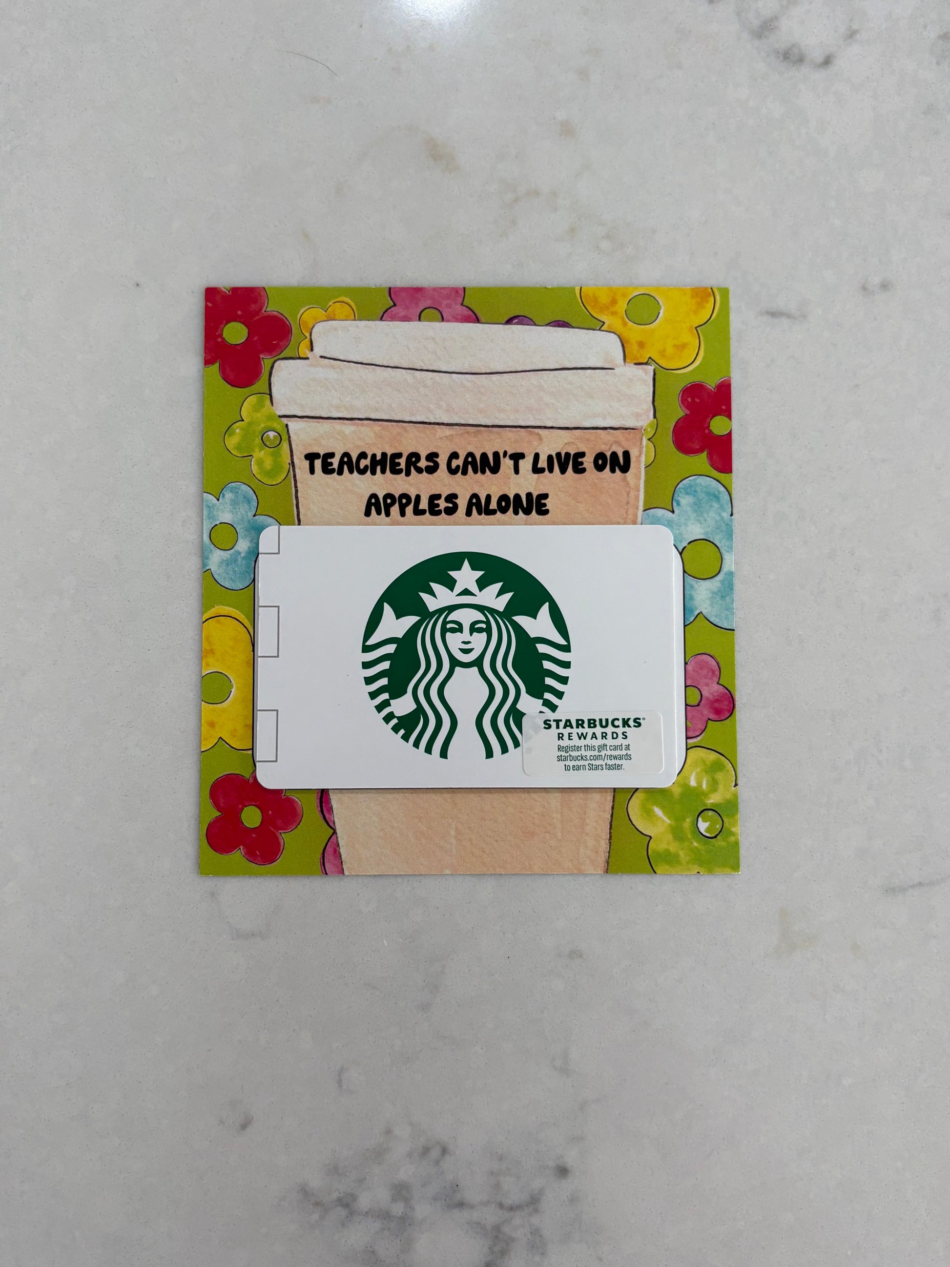 Starbucks gift card with a coffee cup design and text on a floral border, placed on a marble surface.