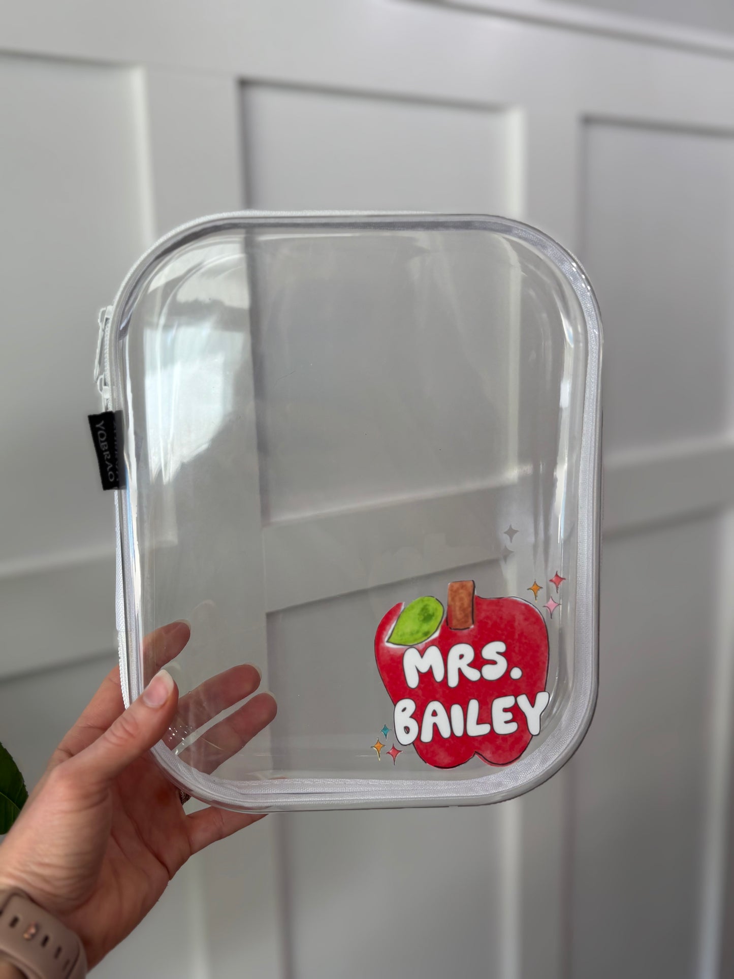 Clear pouch with 'Mrs. Bailey' sticker held by a hand against a white background