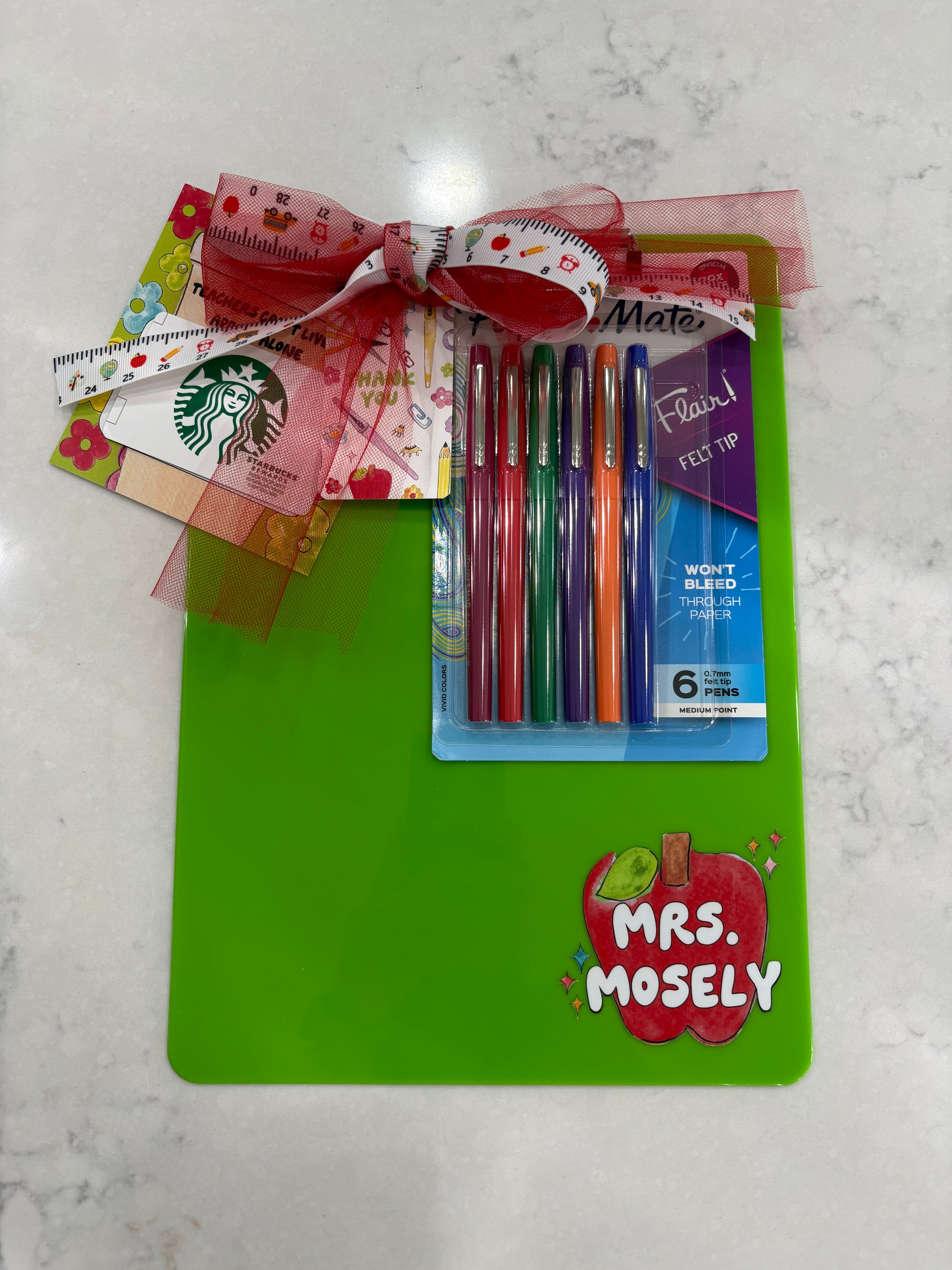 Colorful pens, Starbucks gift card, and and a bow with a "Thank you" tag on a green Clipboard with a personalized apple in the bottom right corner. 