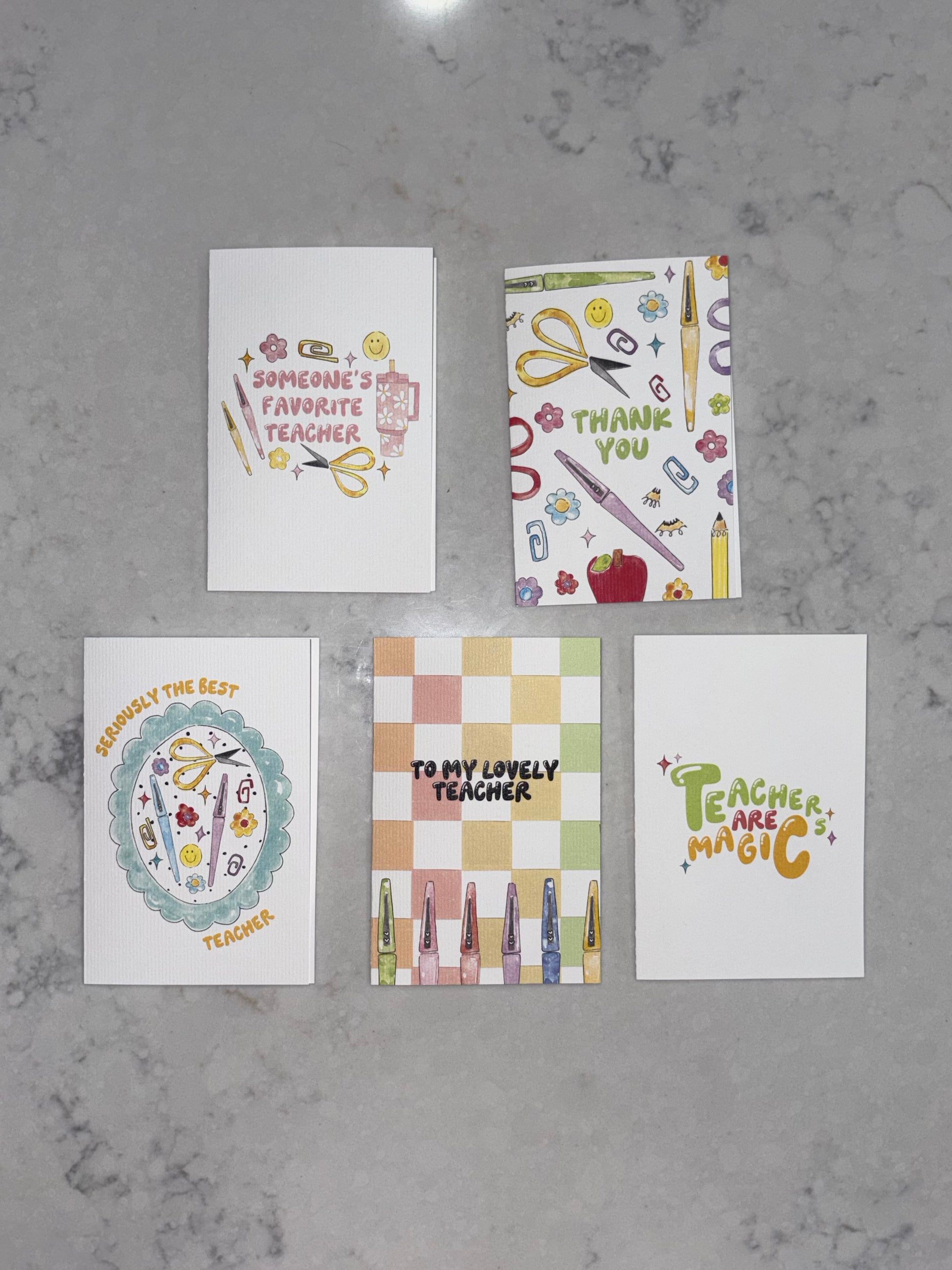 Five greeting cards with teacher-themed designs on a gray surface