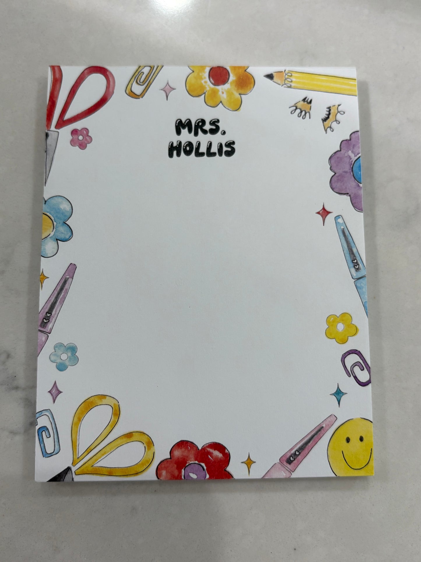 Notebook with colorful illustrations and 'Mrs. Hollis' text on a gray surface