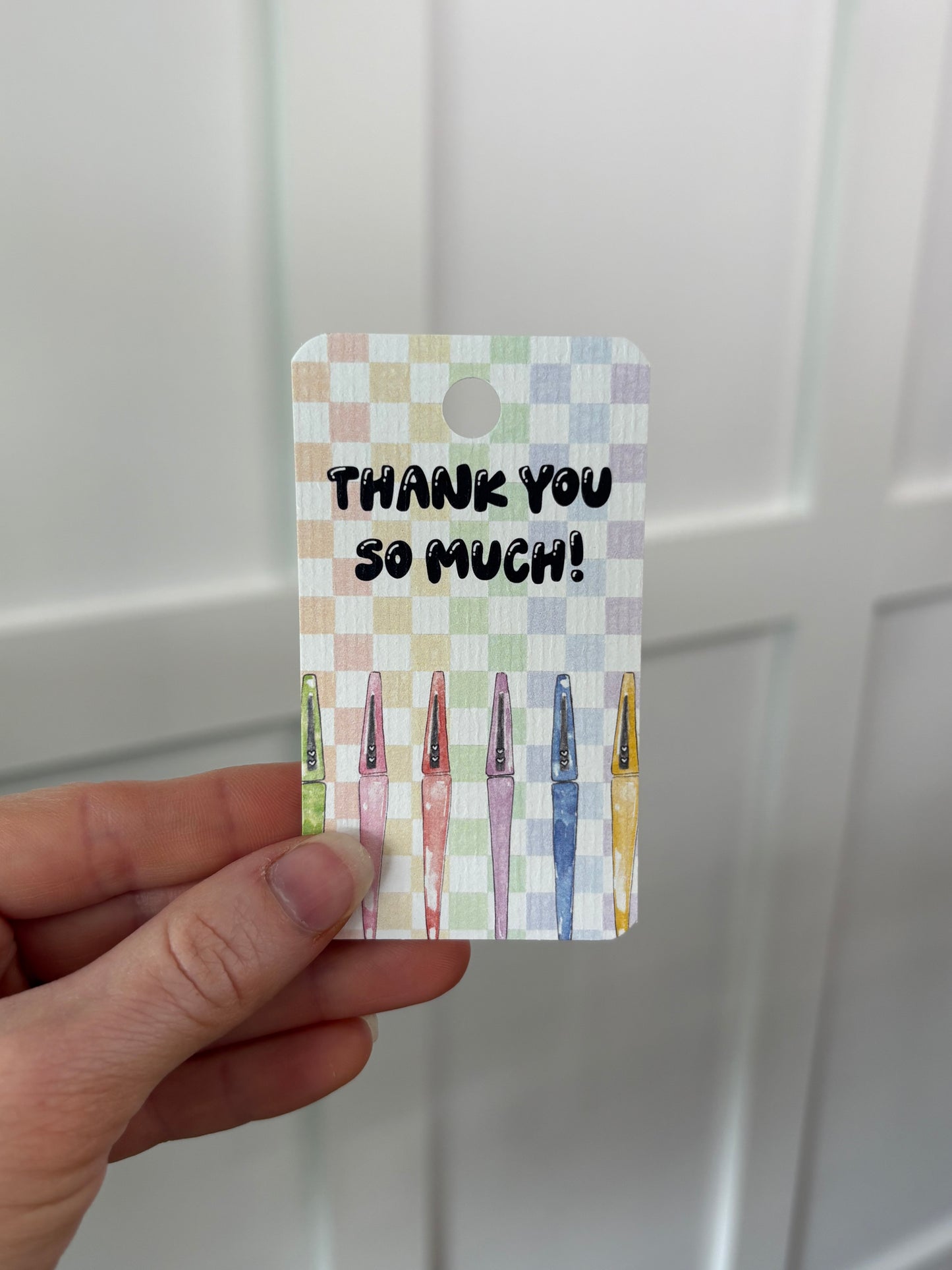 Hand holding a decorative gift tag with 'Thank you so much!' text against a white background
