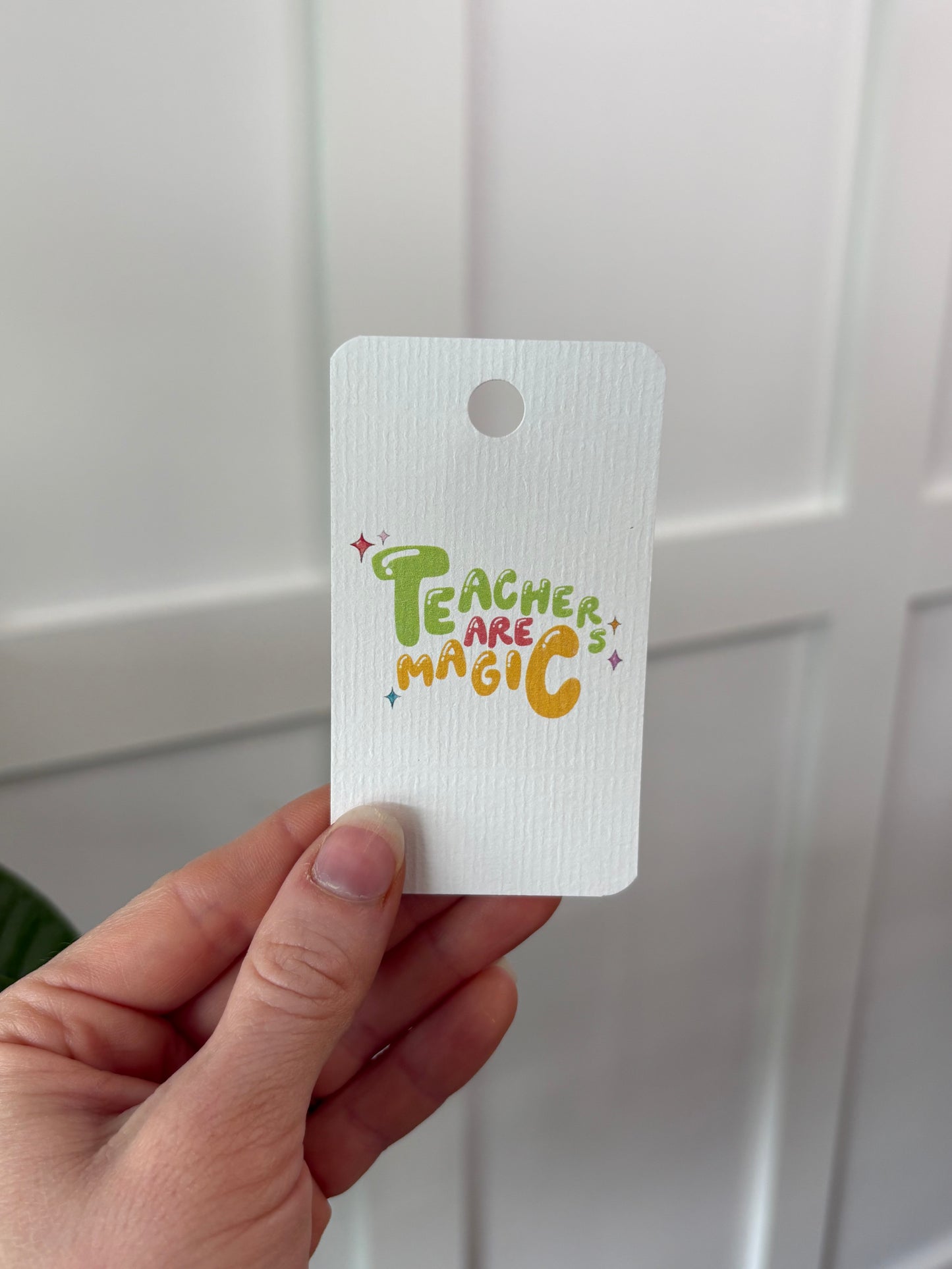 Hand holding a white tag with colorful text and graphics against a white background
