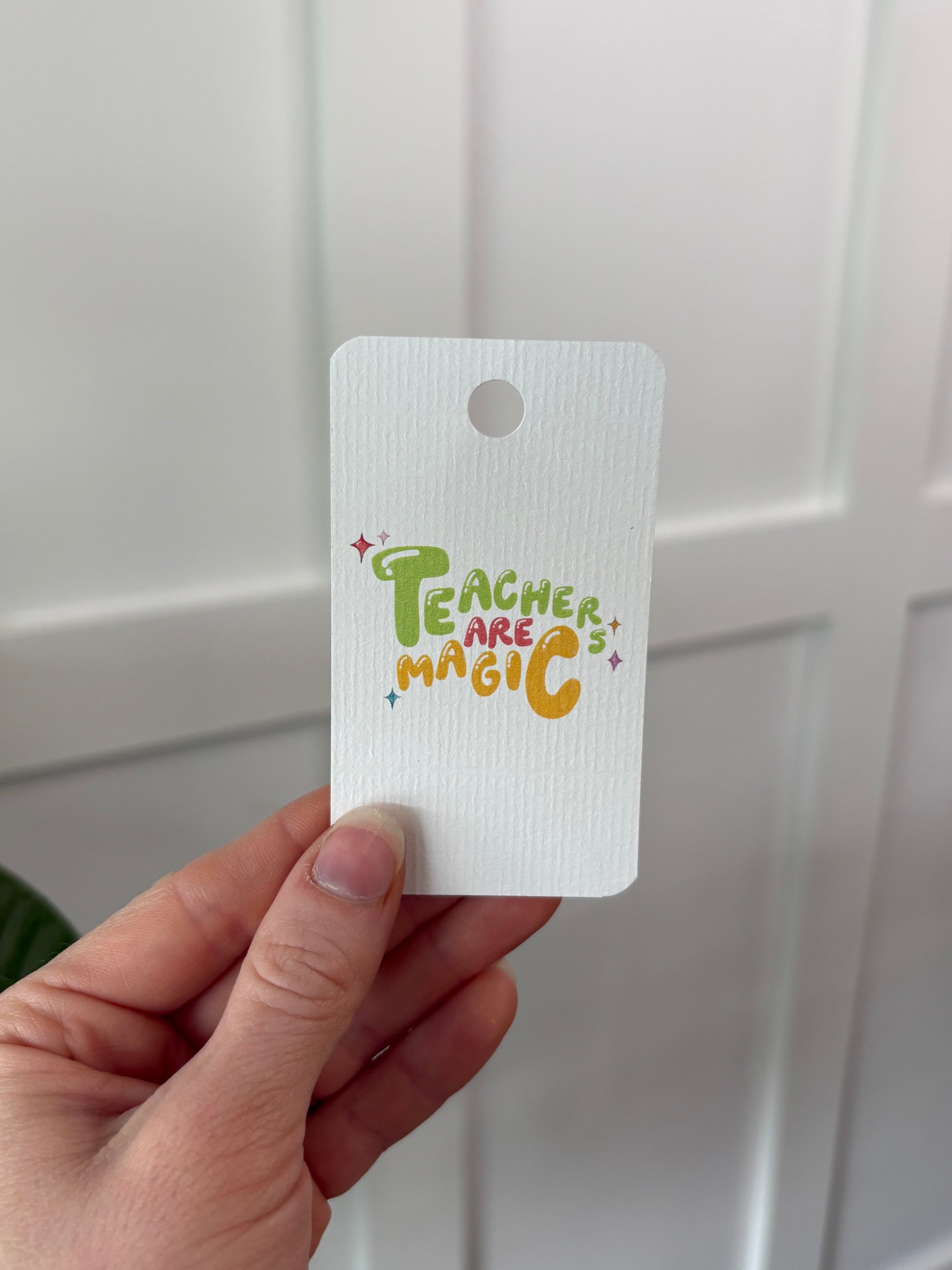 Hand holding a white tag with colorful text and graphics against a white background