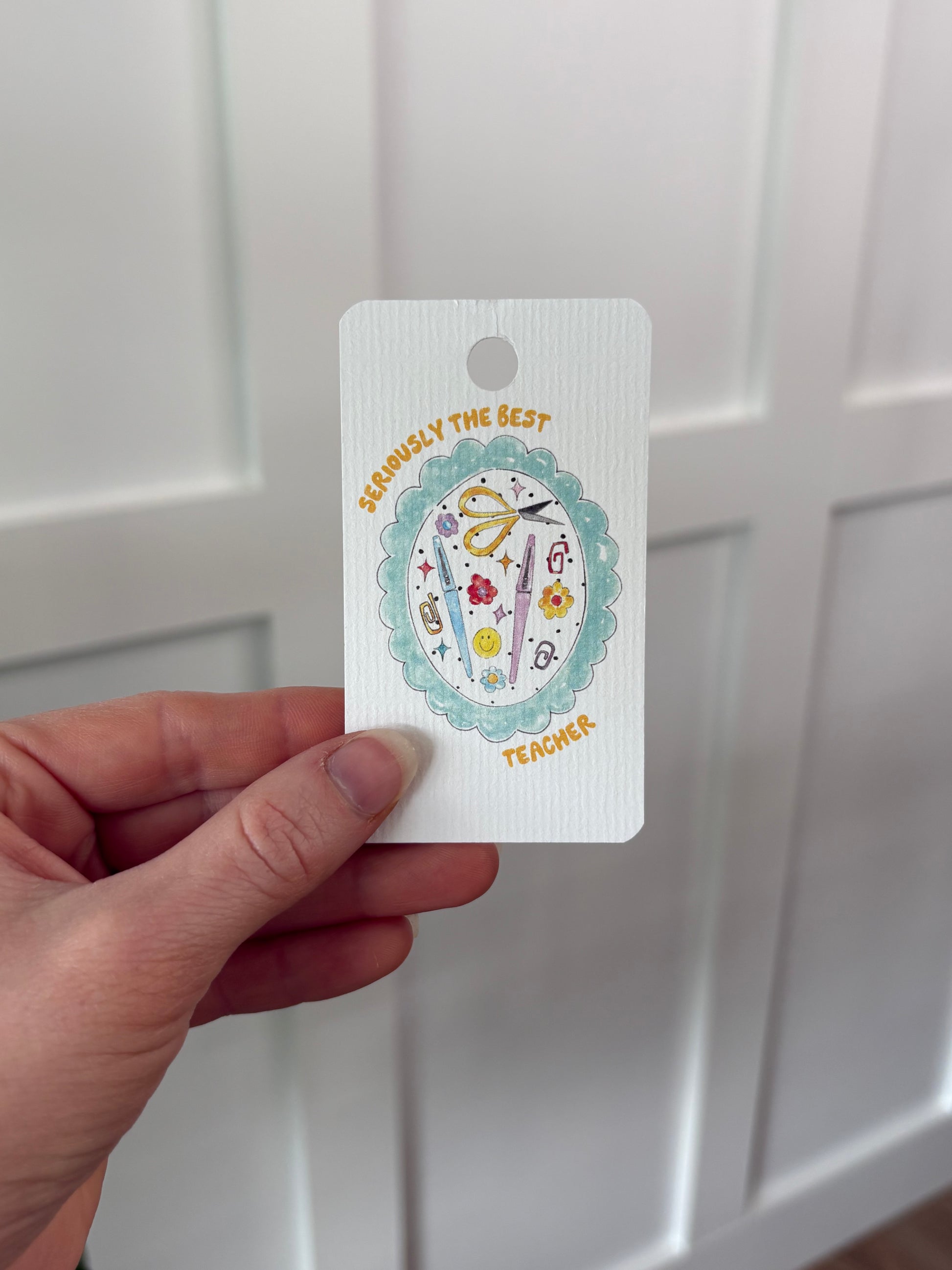 Hand holding a decorative gift tag with illustrations on a white background