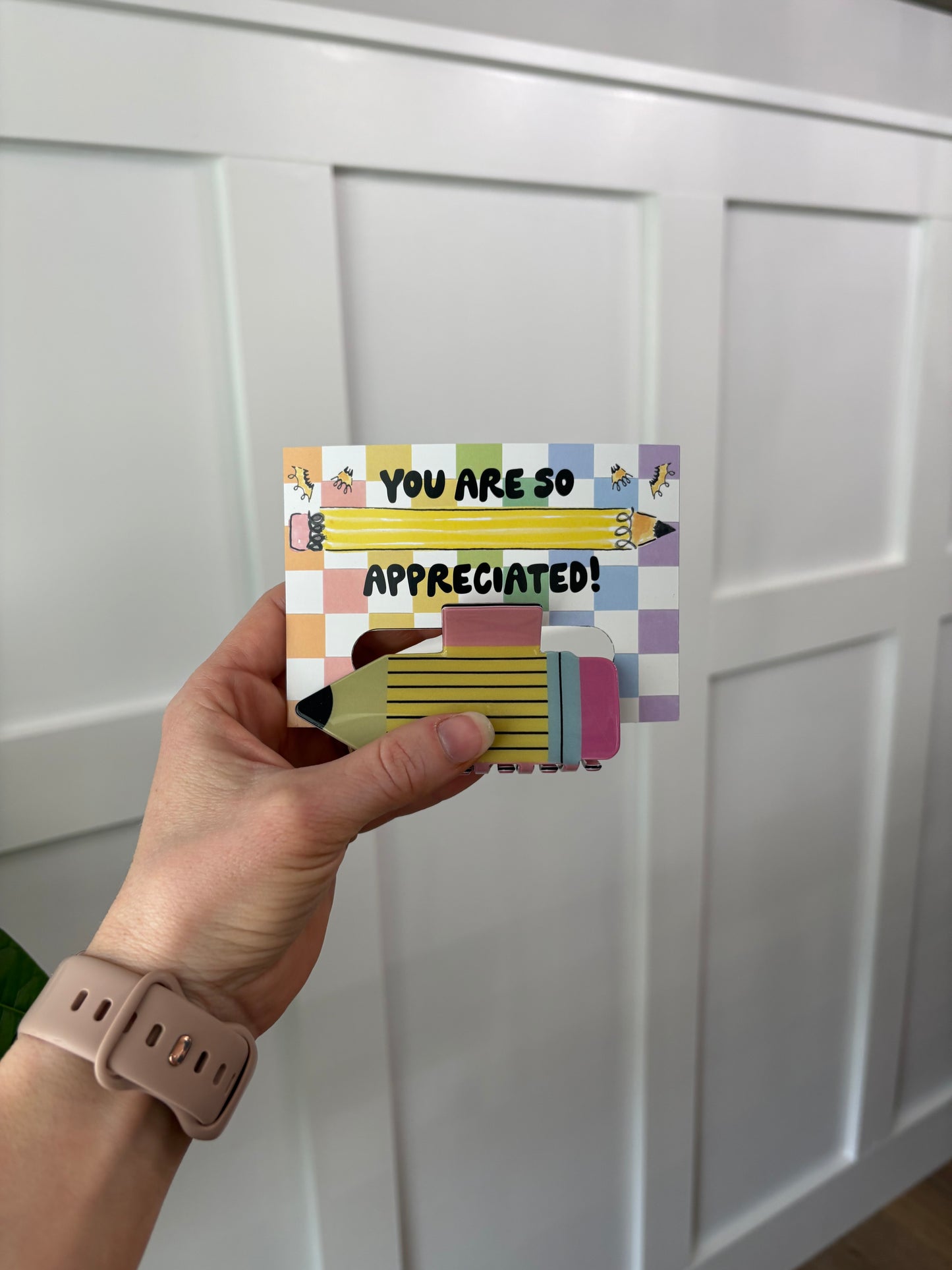 Hand holding a colorful card with text and illustrations against a white door background