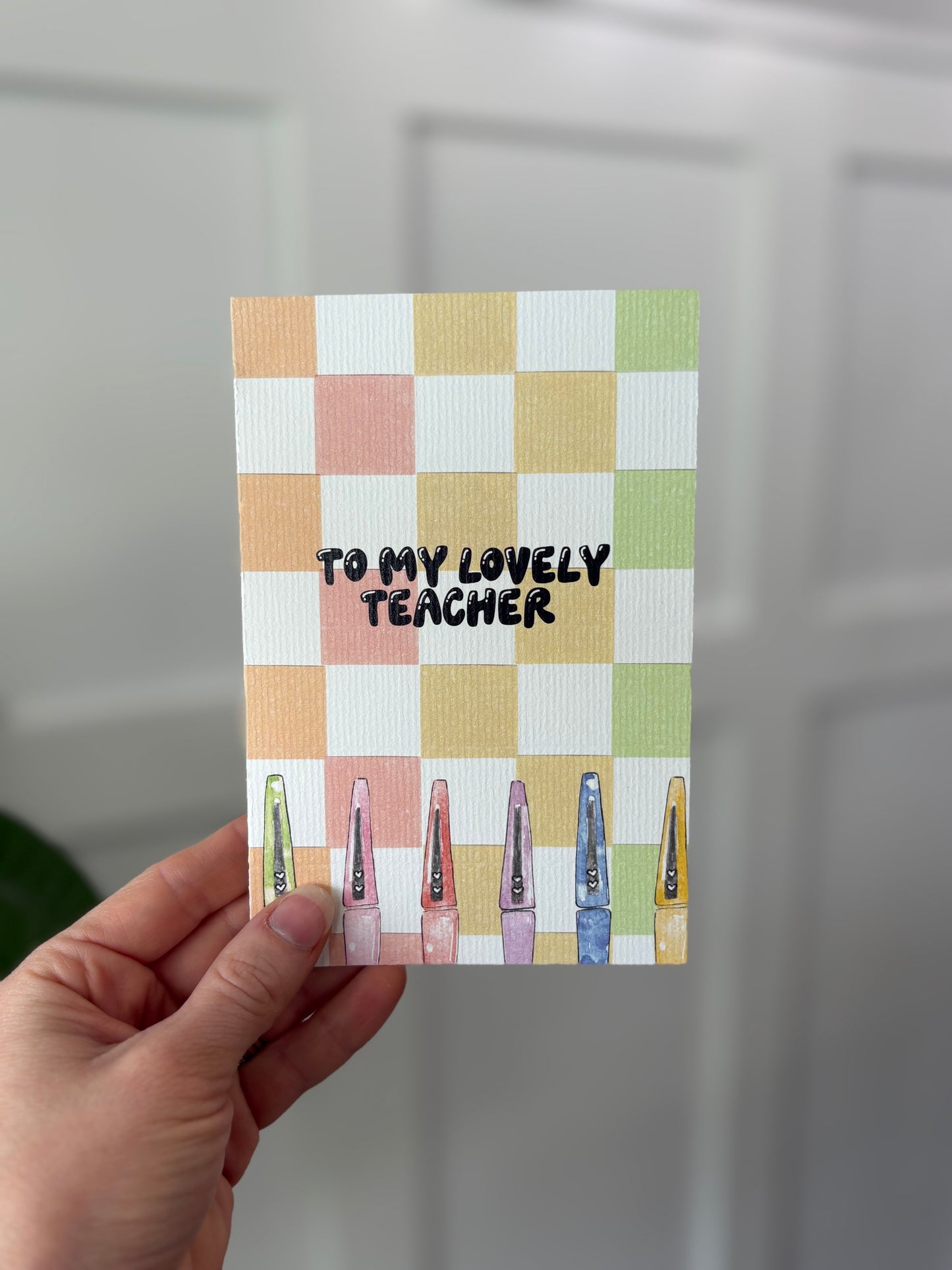 Card with 'To my lovely teacher' text on a checkered background held by a hand.