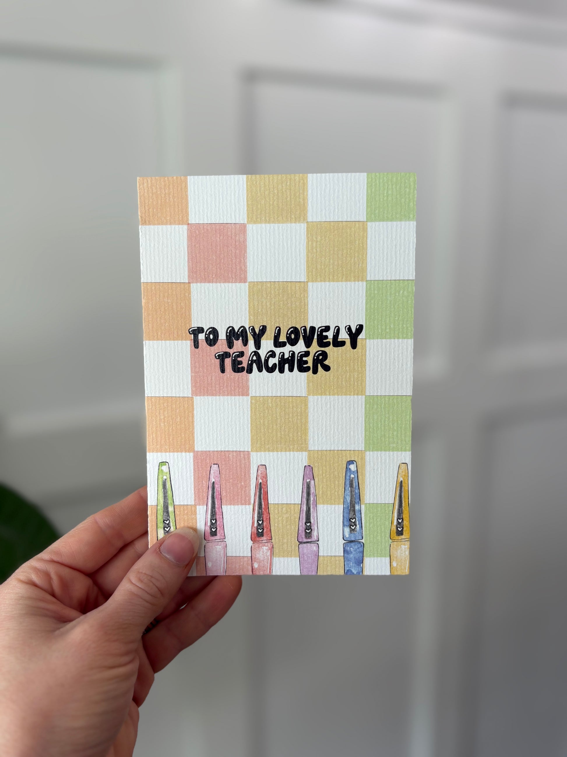 Card with 'To my lovely teacher' text on a checkered background held by a hand.