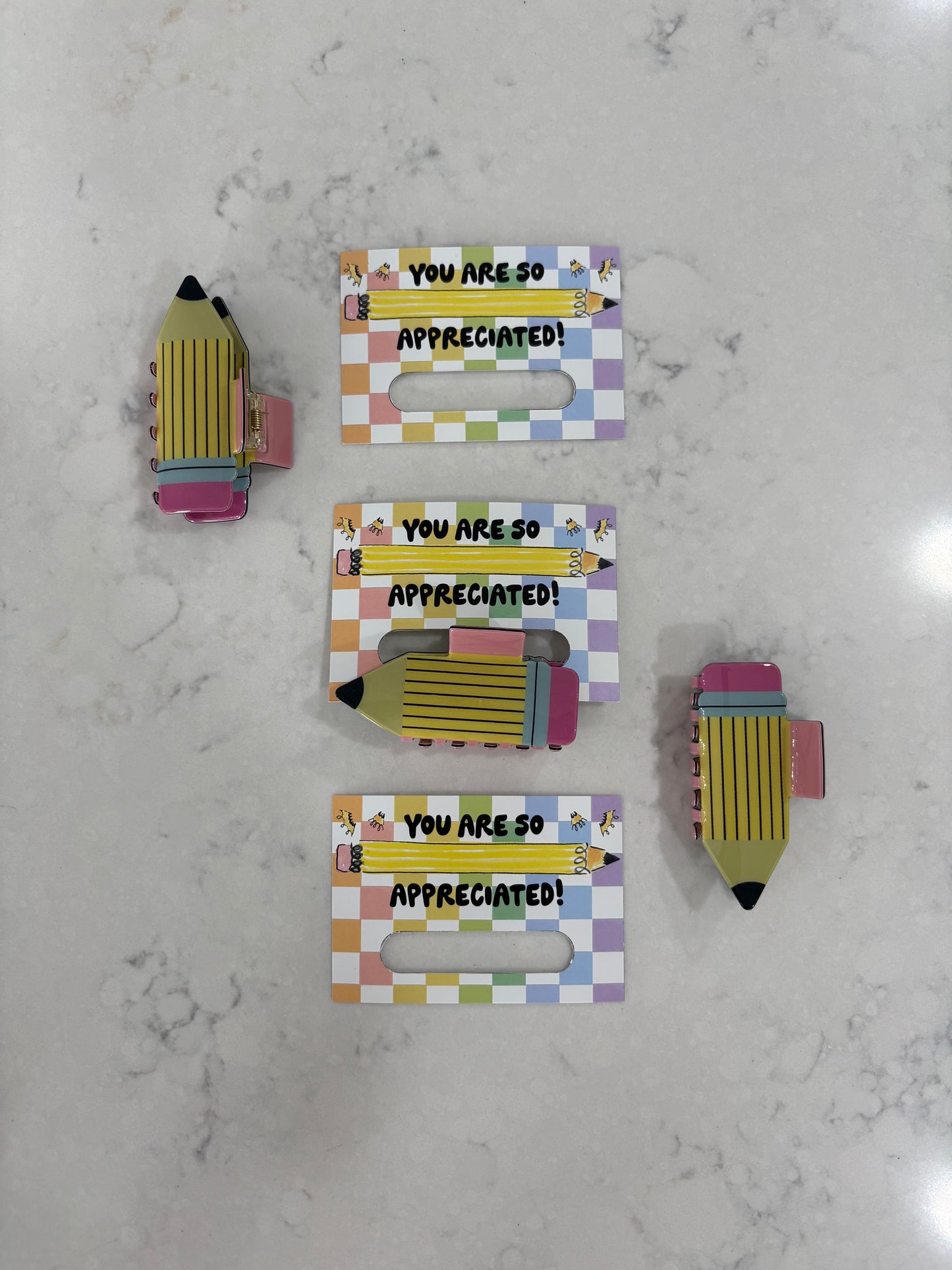 Pencil hair clips held by a colorful holder with 'You are so appreciated!' text on a marble surface