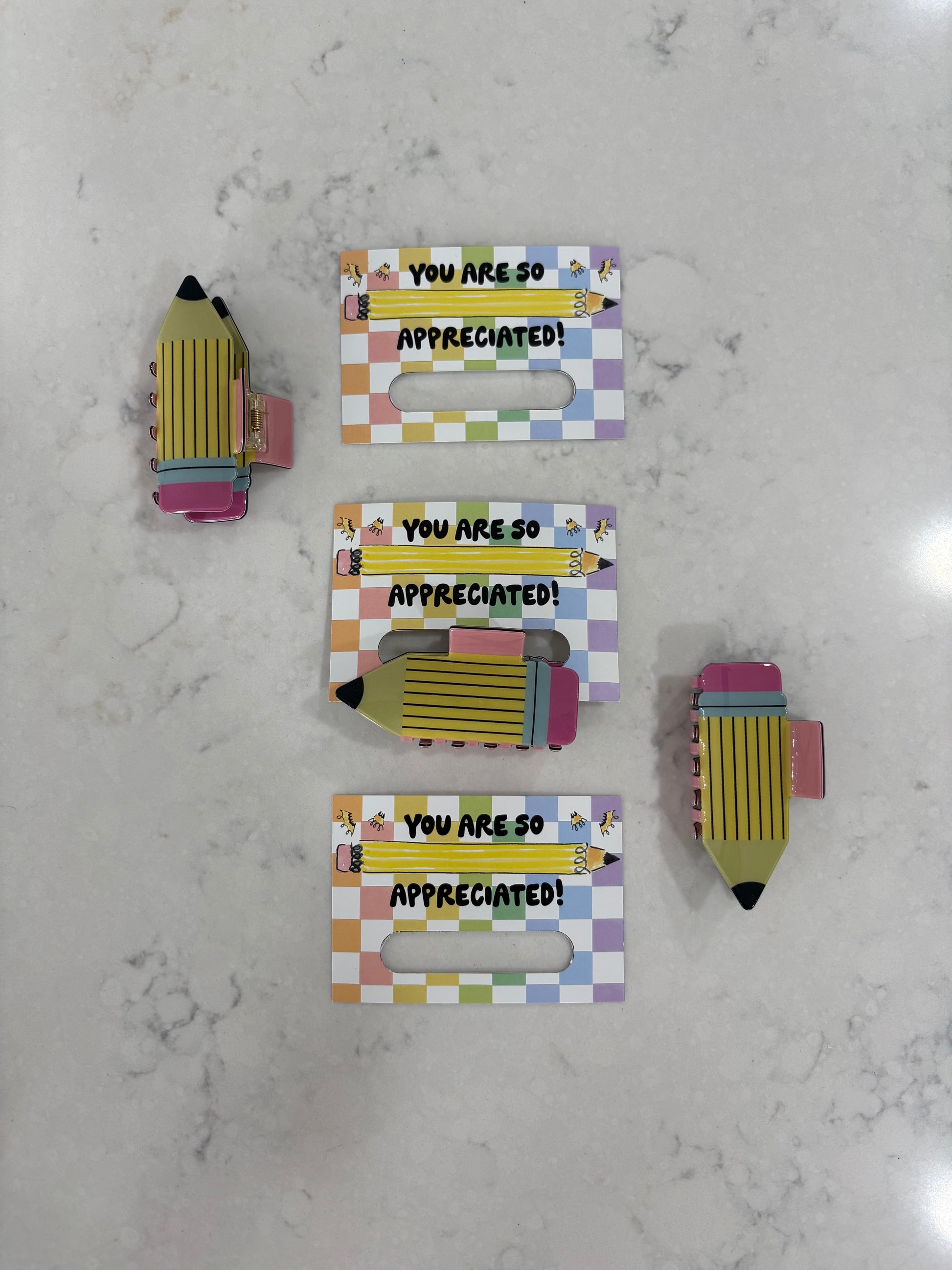 Pencil hair clips held by a colorful holder with 'You are so appreciated!' text on a marble surface
