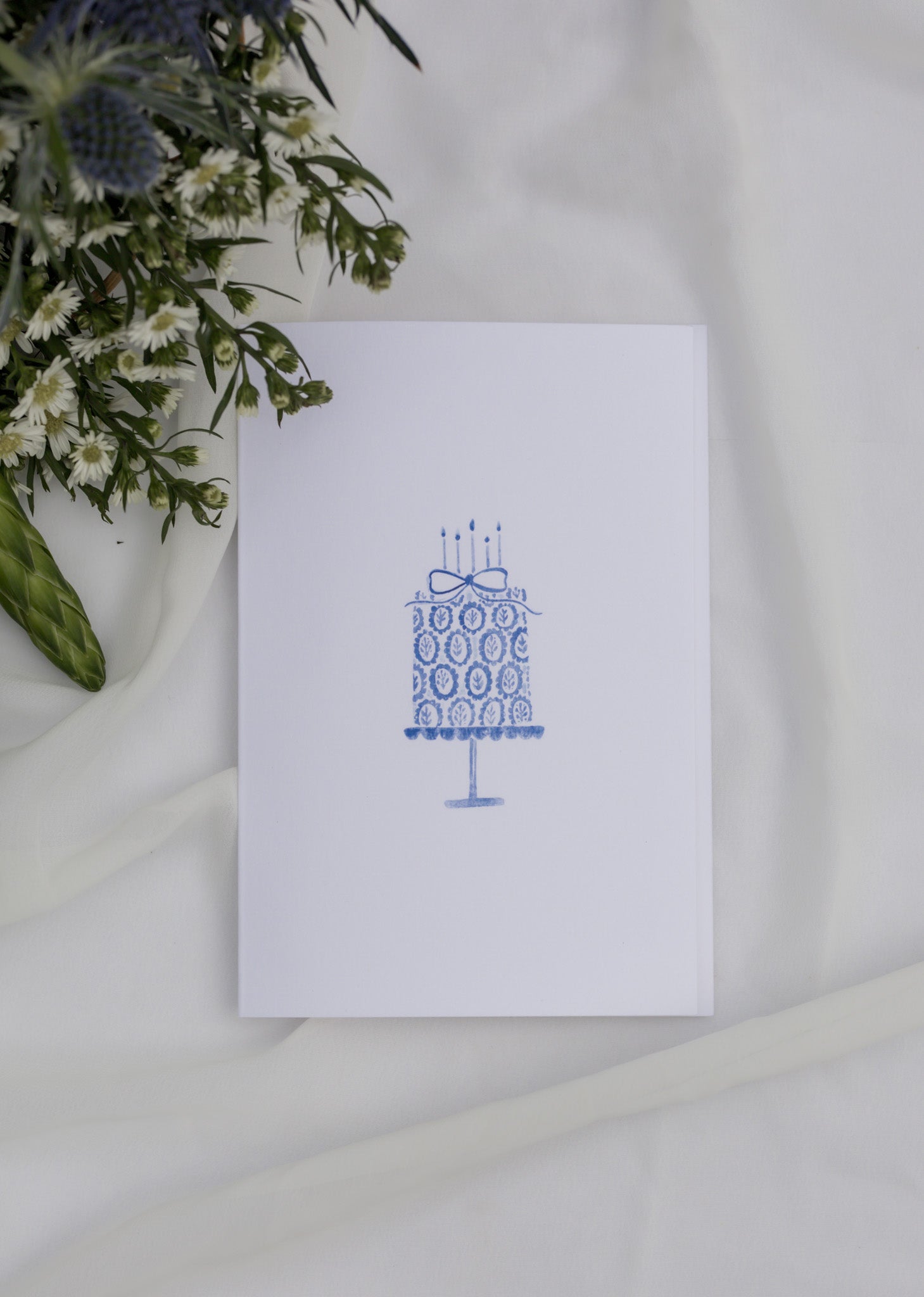 White card with blue patterned design on a white surface with greenery.