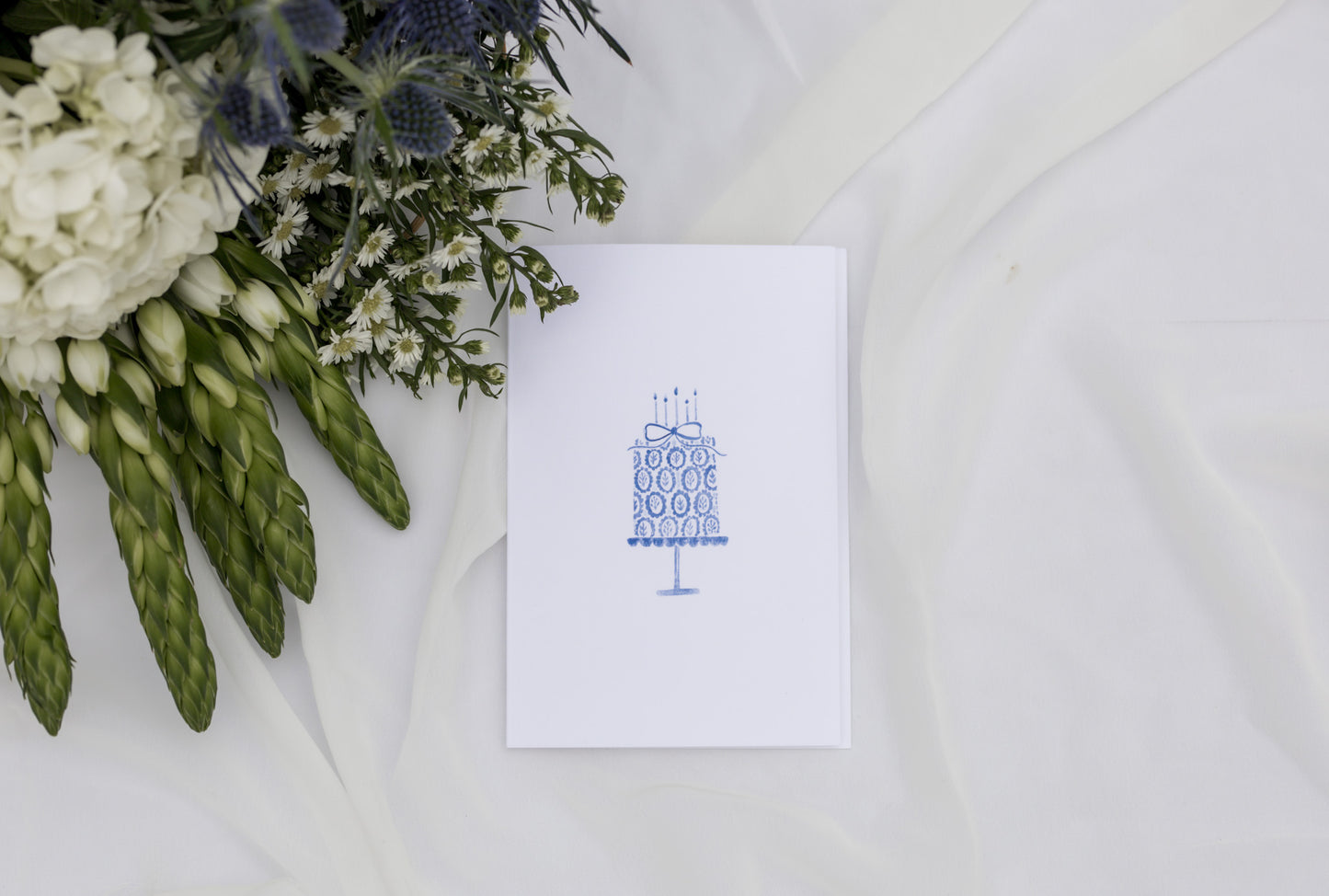 White card with blue design next to a bouquet of flowers on a white background