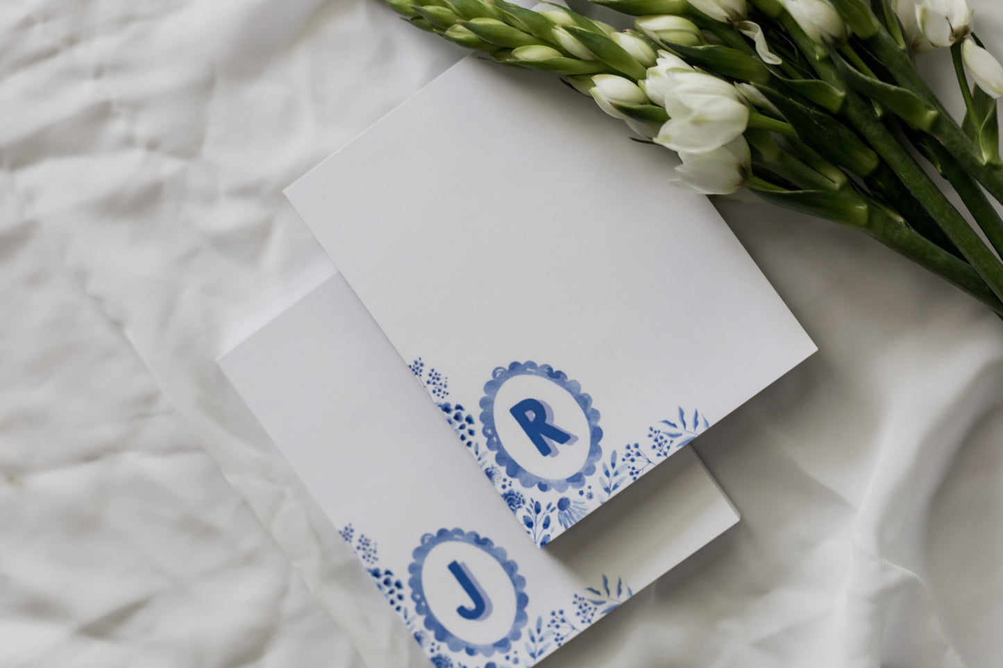 memo pads with initials and floral design on a white fabric background with flower arrangement 