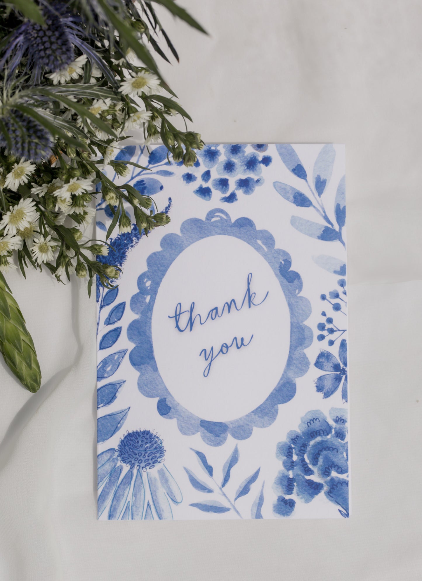 Blue floral card with 'thank you' text on a white background with a flower arrangement. 