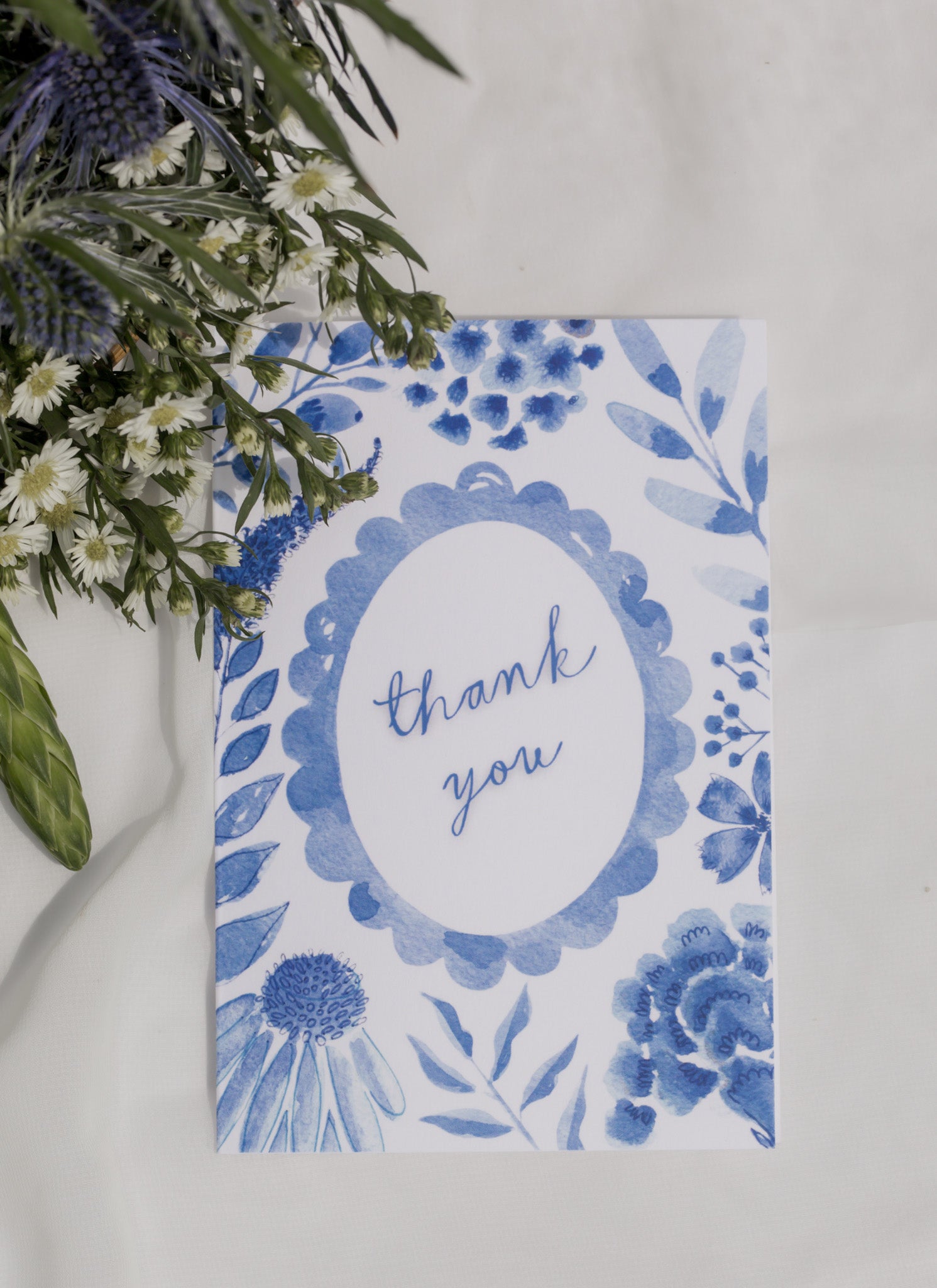 Blue floral card with 'thank you' text on a white background with a flower arrangement. 