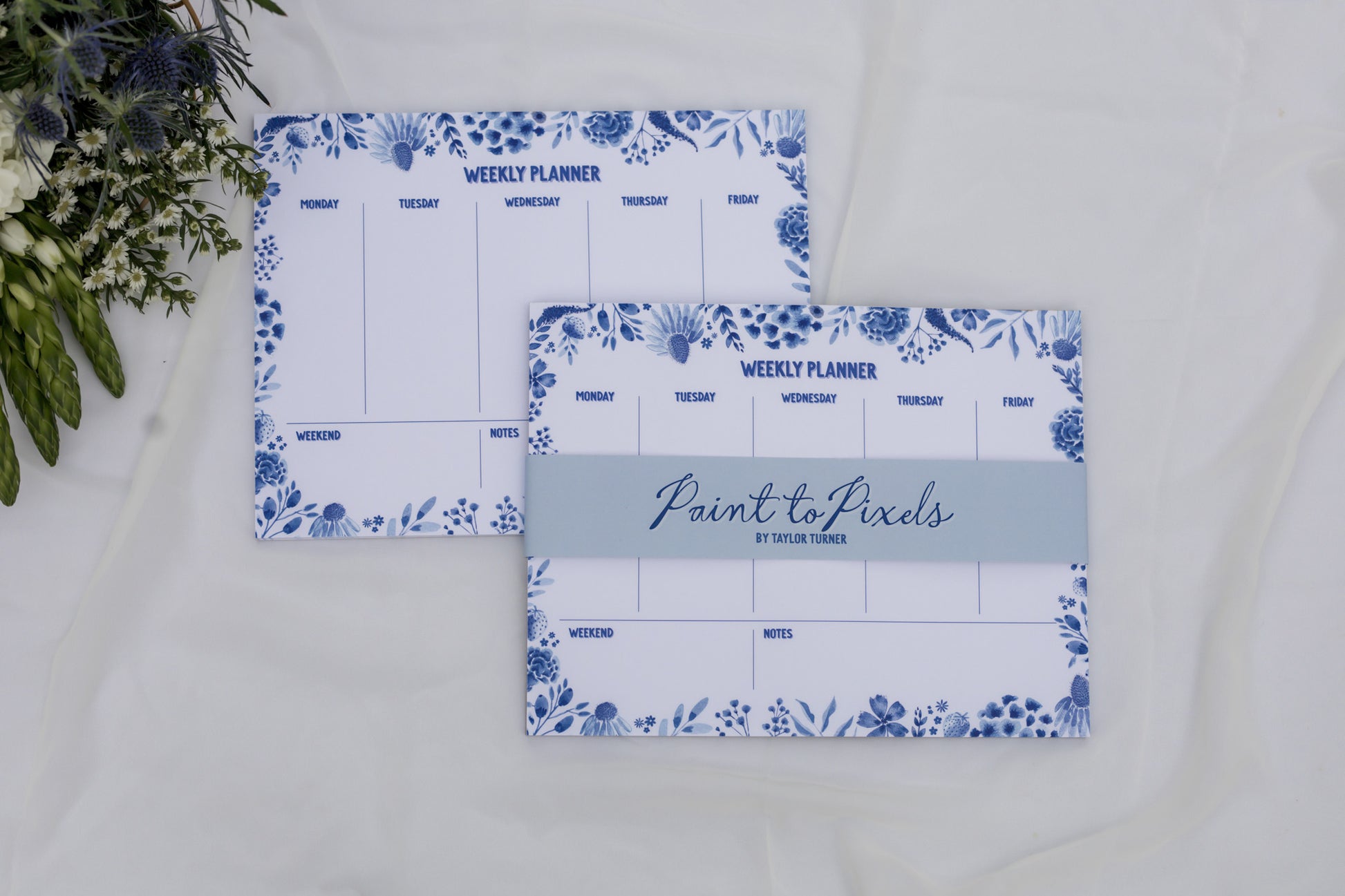 Two weekly planners with floral designs on a white surface.