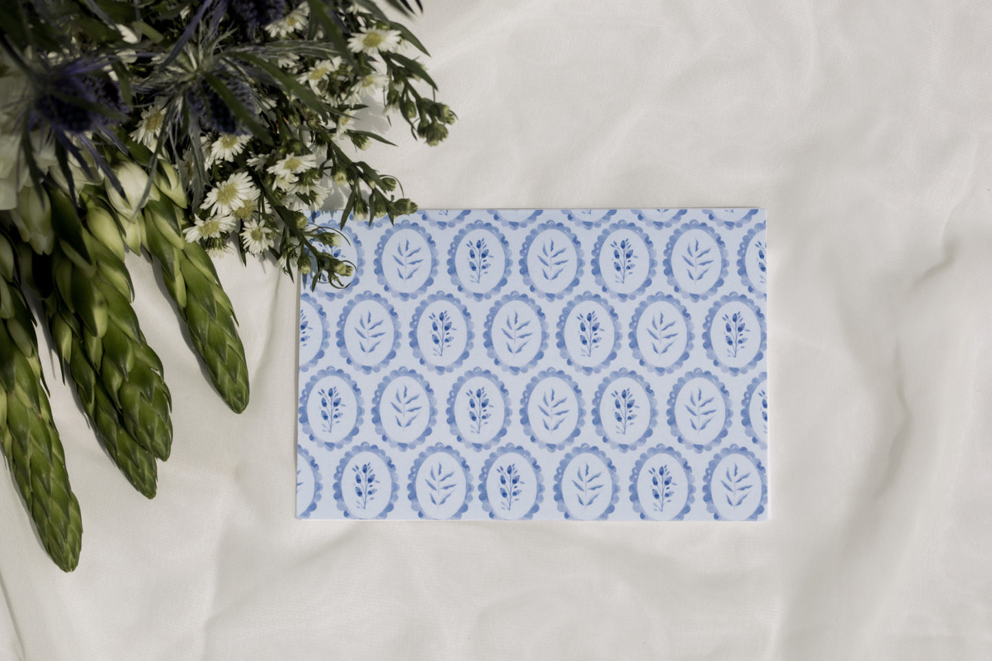 Blue patterned card on a white surface with greenery