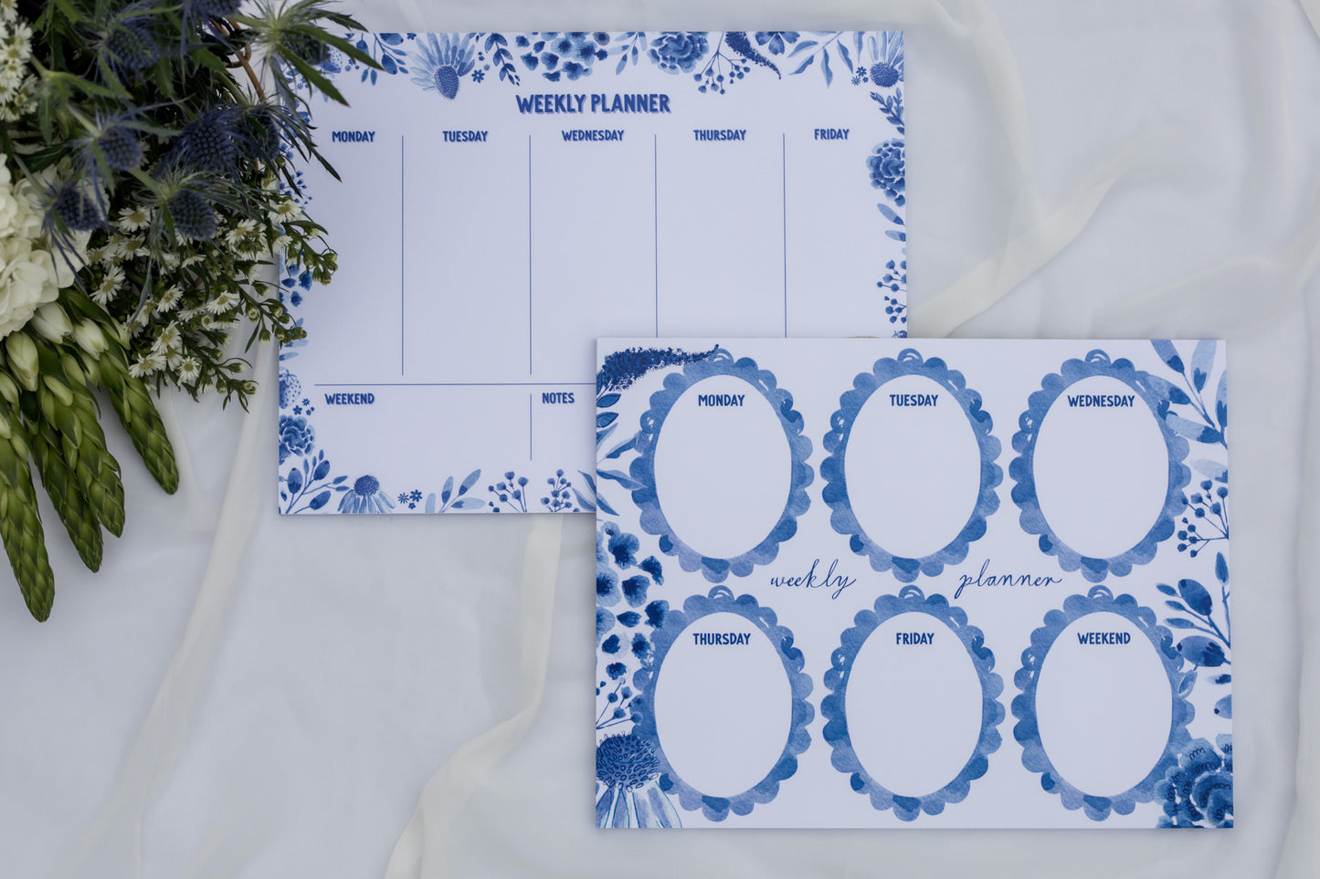 Two blue and white weekly planners with floral designs on a white surface.