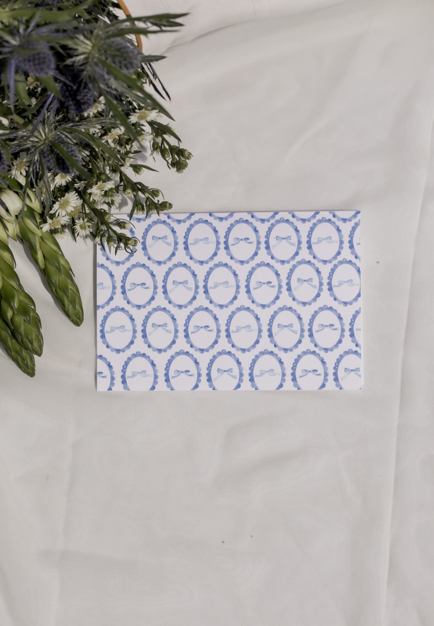 Decorative card with blue circular patterned bows on a white surface with flowers in the background