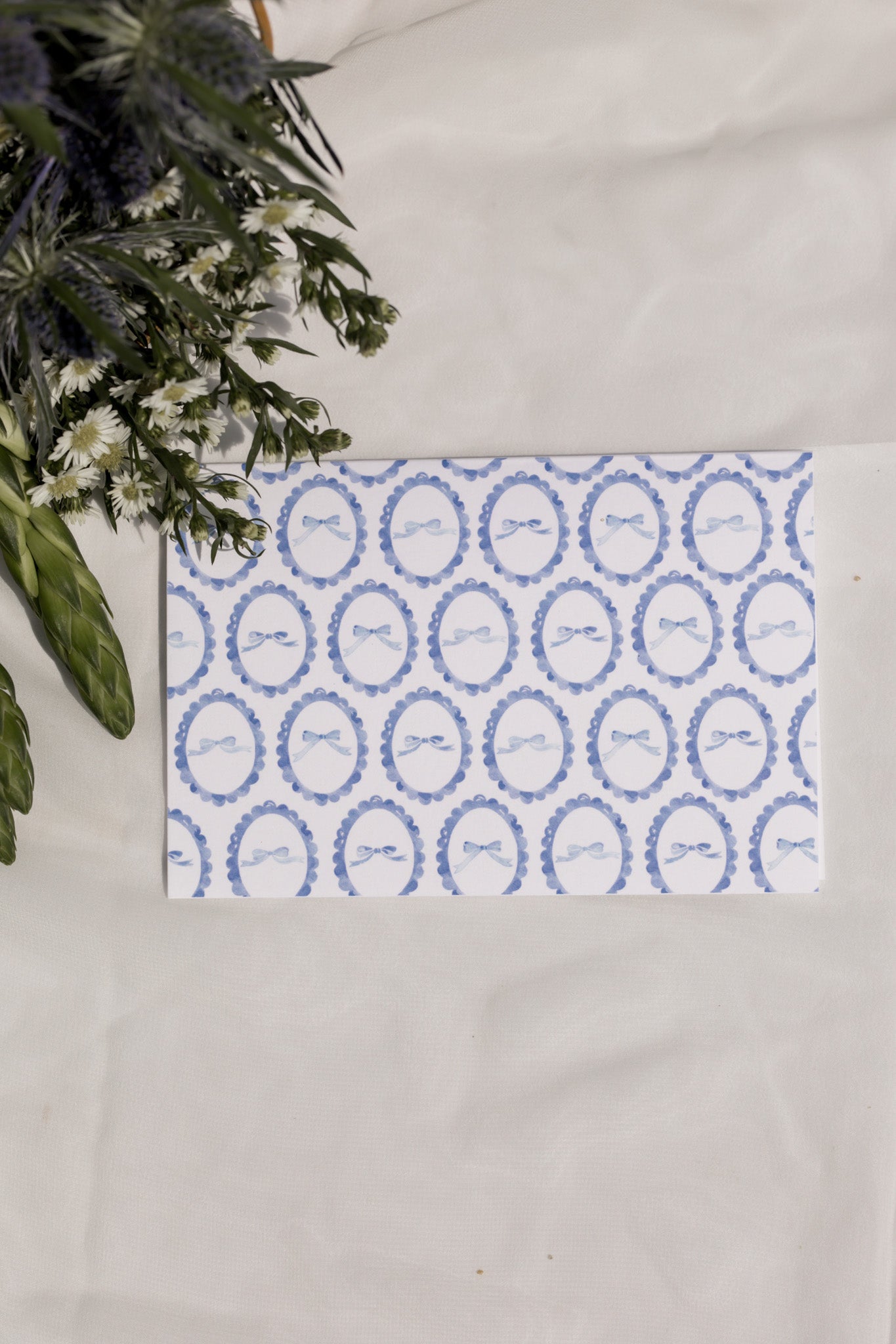 Decorative card with blue circular patterned bows on a white surface with flowers in the background