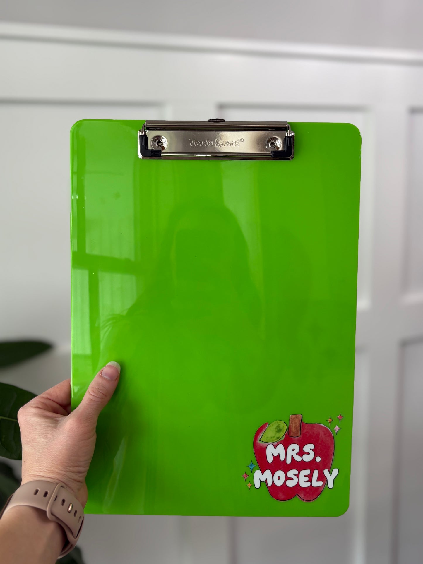Green clipboard with 'Mrs. Moseley' logo held by a hand against a white wall.