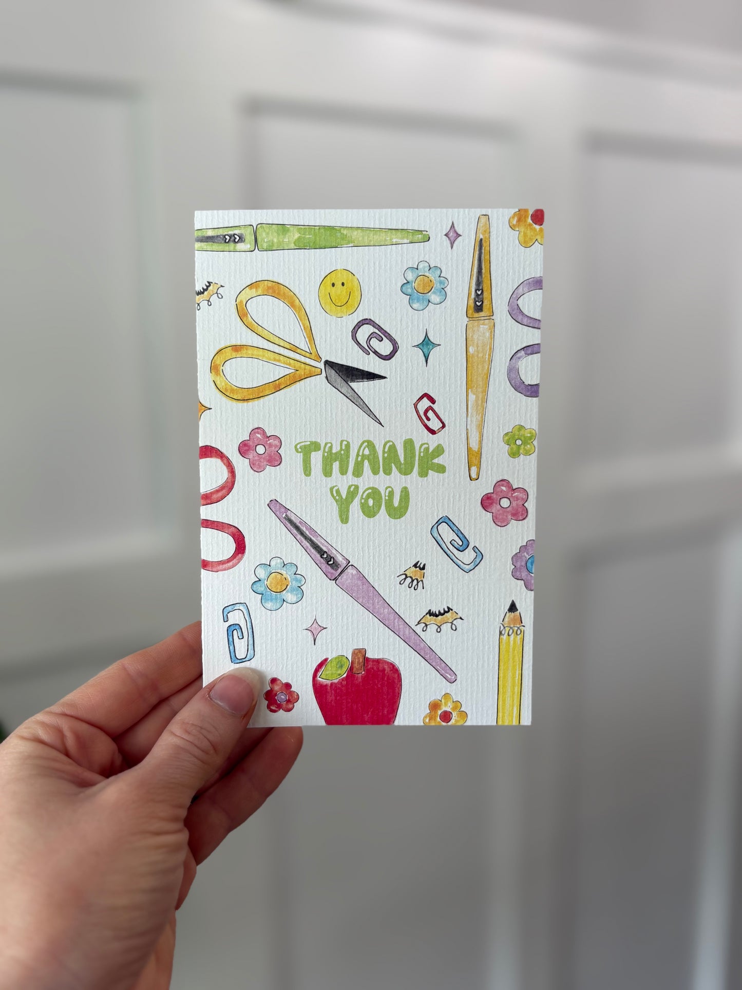 Hand holding a card with stationery-themed illustrations and 'Thank You' text.