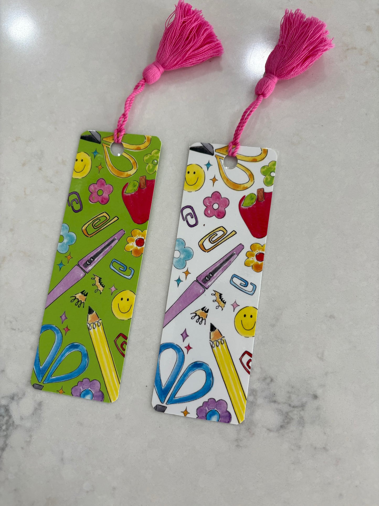Two colorful bookmarks with illustrations of school supplies on a light gray surface.