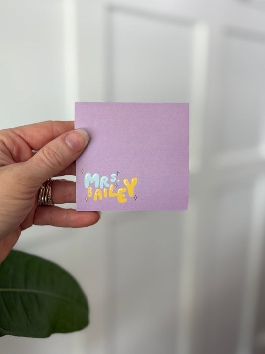 Hand holding a purple sticky notepad with 'Mr Bailey' text against a white background