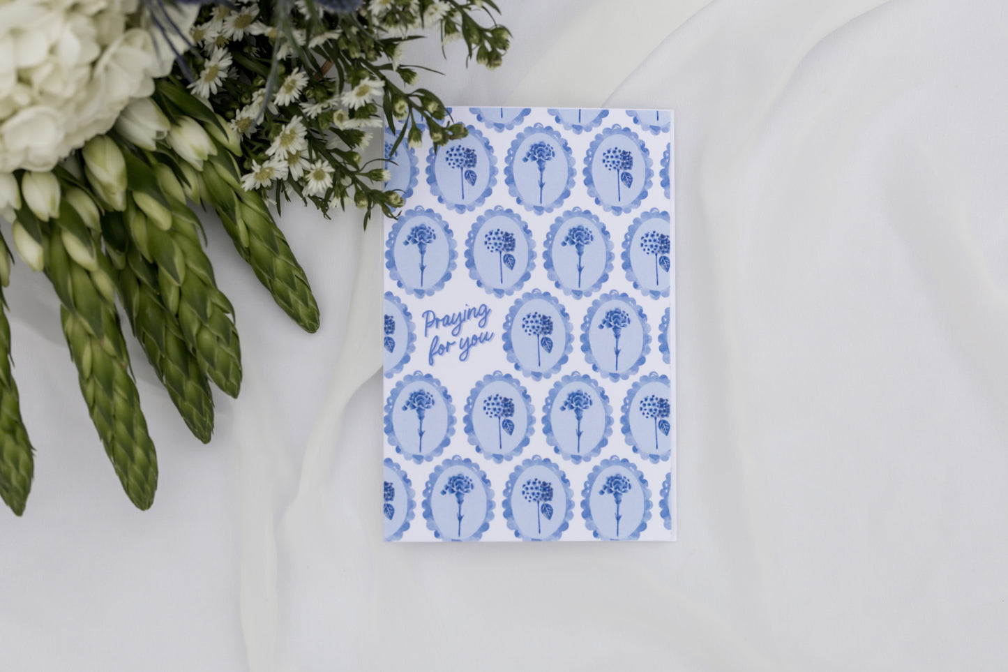 Greeting card with blue floral pattern and text next to asparagus and flowers on a white surface
