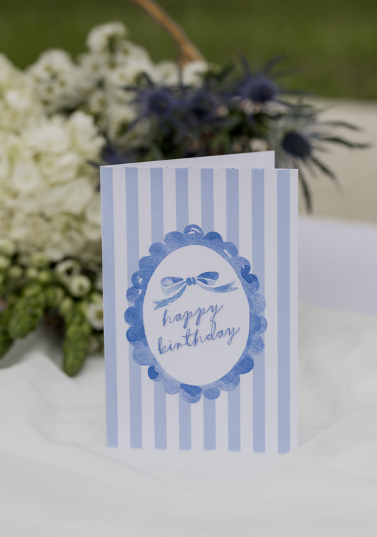 Blue birthday card with decorative elements on a white surface with flowers in the background