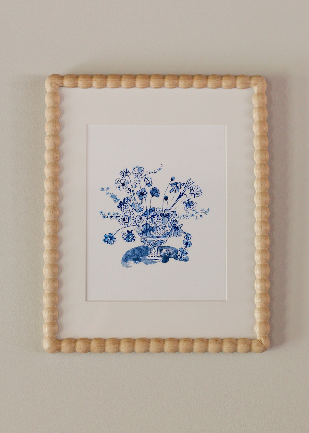 Blue bouquet arrangement beneath a white matte in a wooden textured frame against a neutral background. 