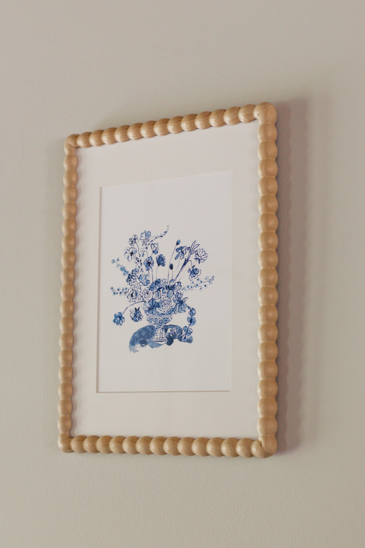 Blue bouquet arrangement beneath a white matte in a wooden textured frame against a neutral background. 