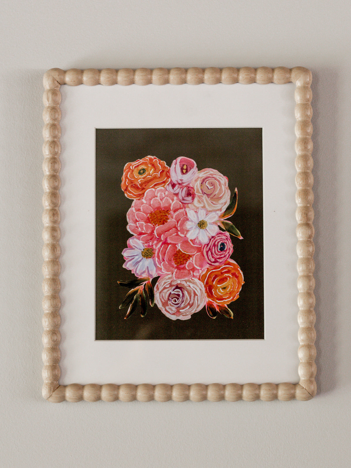 A framed floral art print featuring pink and orange roses on a dark background, set within a white mat and a light beige beaded wooden frame, mounted on a neutral wall.