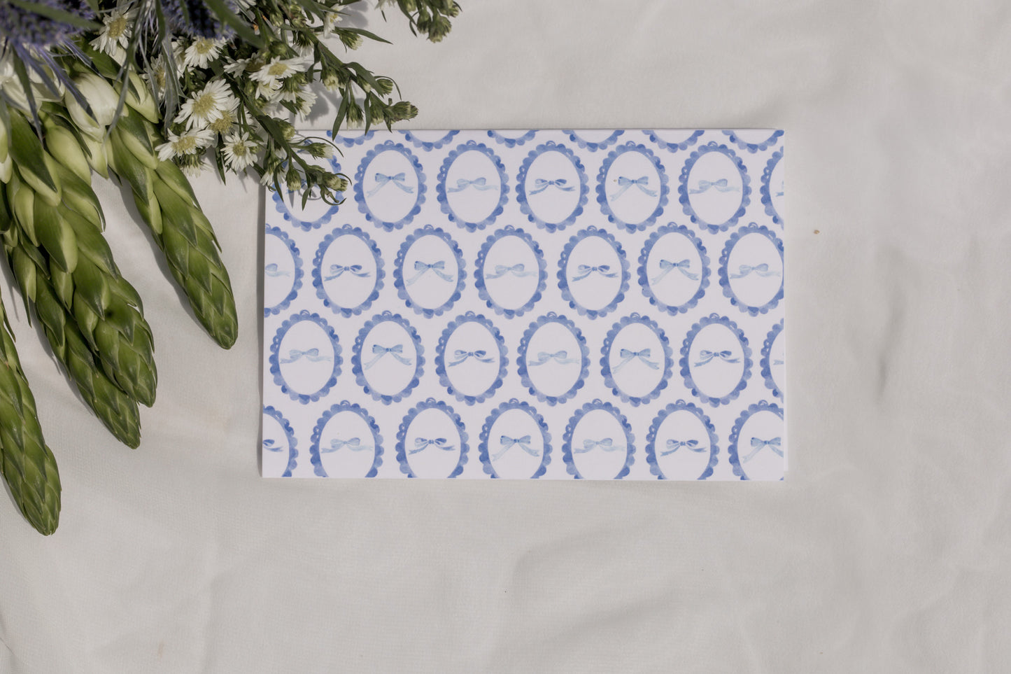 Decorative card with blue circular patterned bows on a white surface with flowers in the background