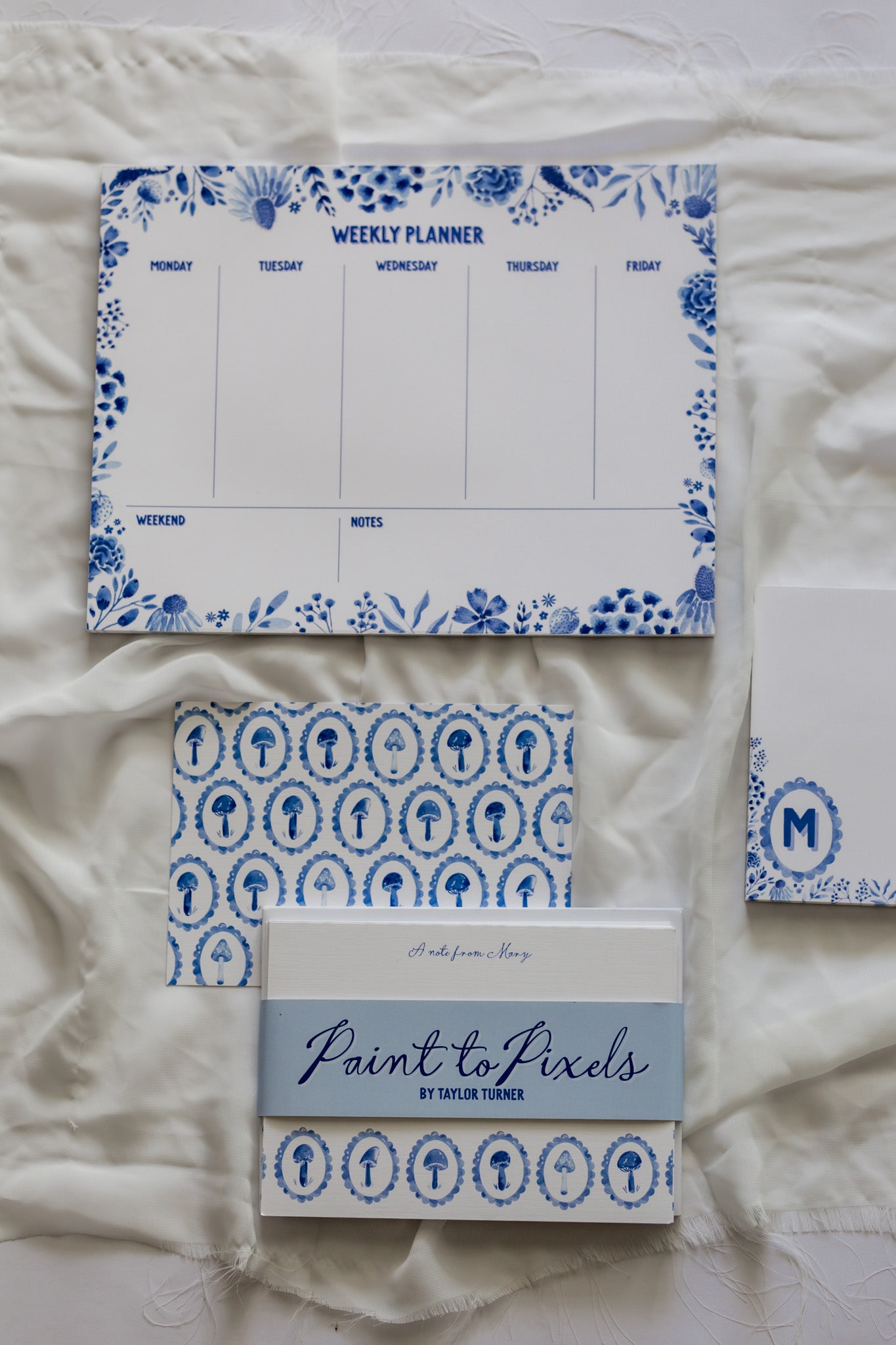 Weekly planner and patterned stationery cards with 'Paint to Pixels' branding on a white fabric background