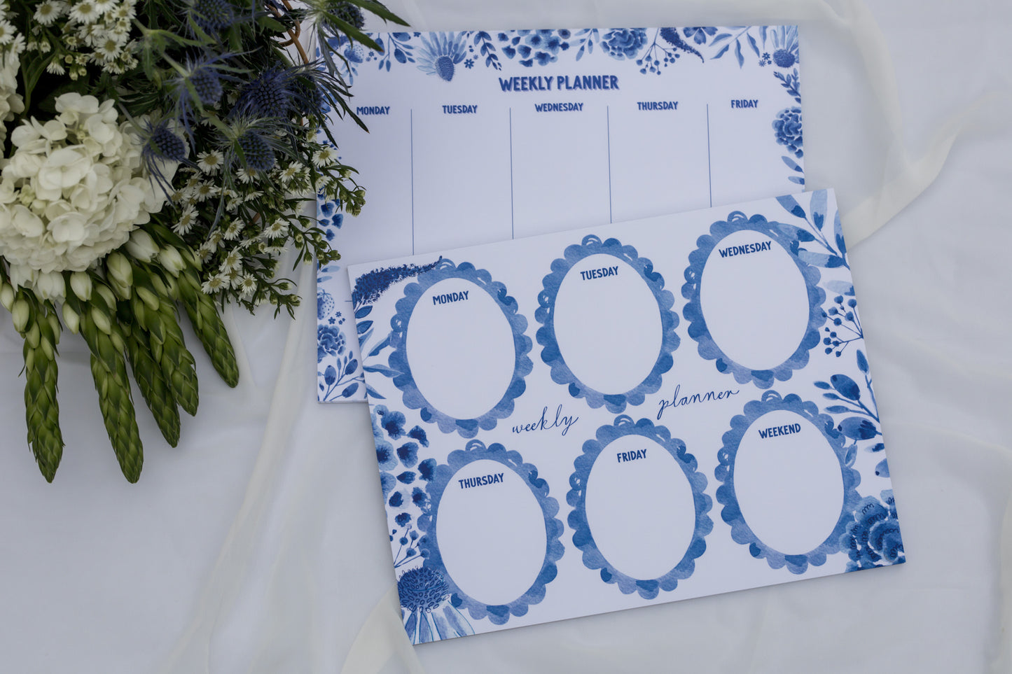 Weekly planner with blue floral design on a white surface with flowers.