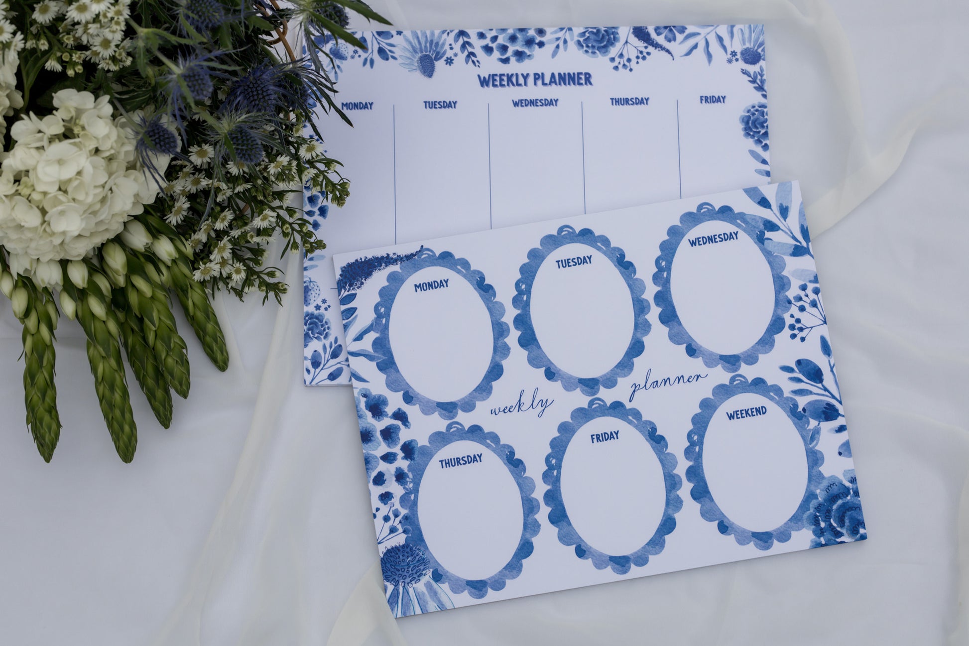 Weekly planner with blue floral design on a white surface with flowers.