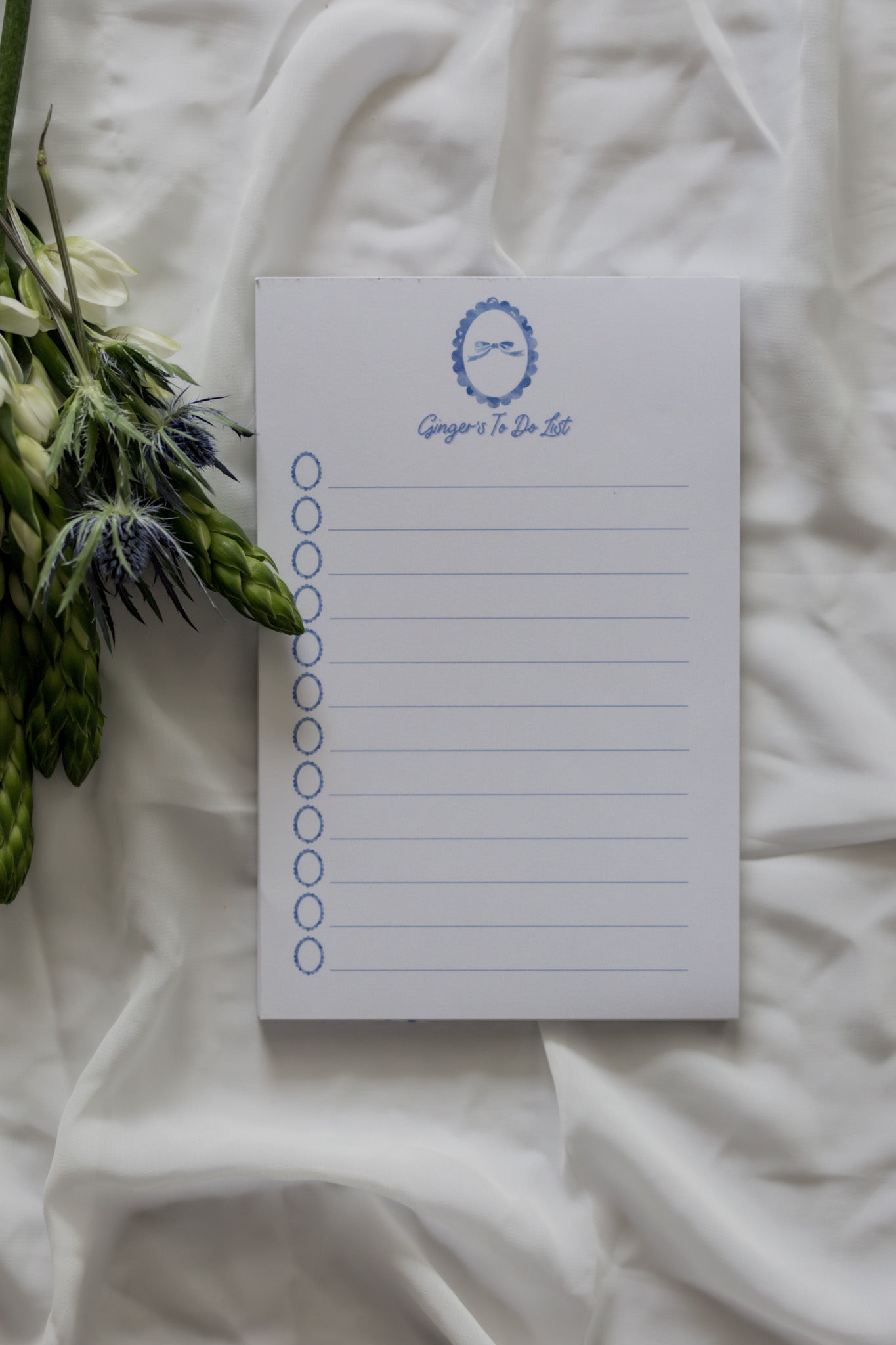 Blue notepad with a bow at the top on a white background with a flower arrangement 