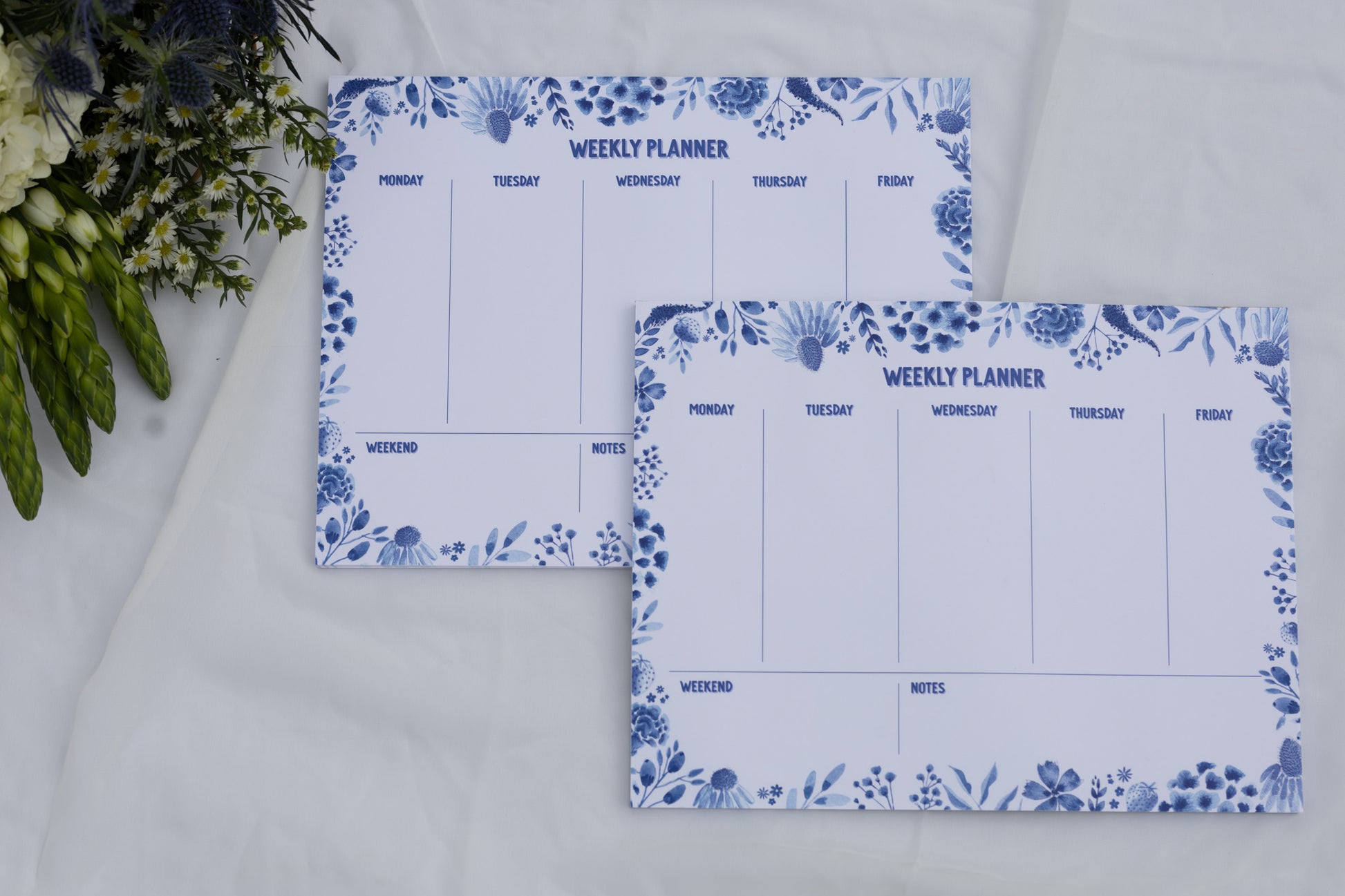 Two weekly planners with floral designs on a white surface.