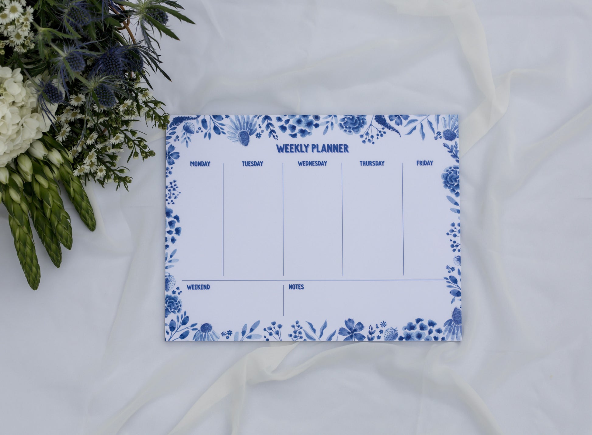 Weekly planner with floral design on a white surface with flowers.